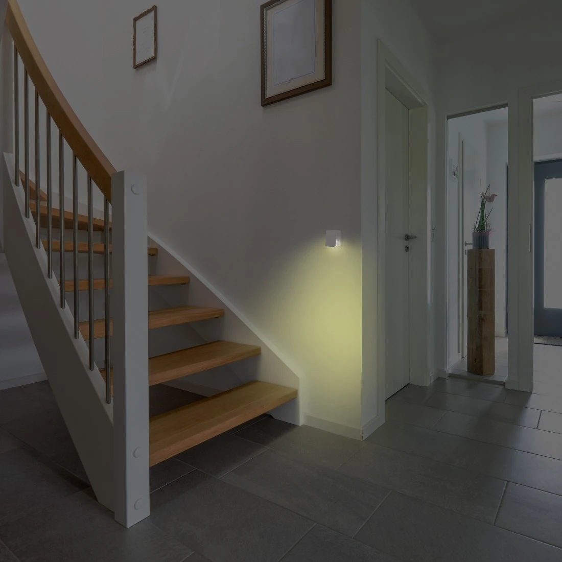 Un corridoio illuminato con scale. Una piccola luce quadrata sulla parete.