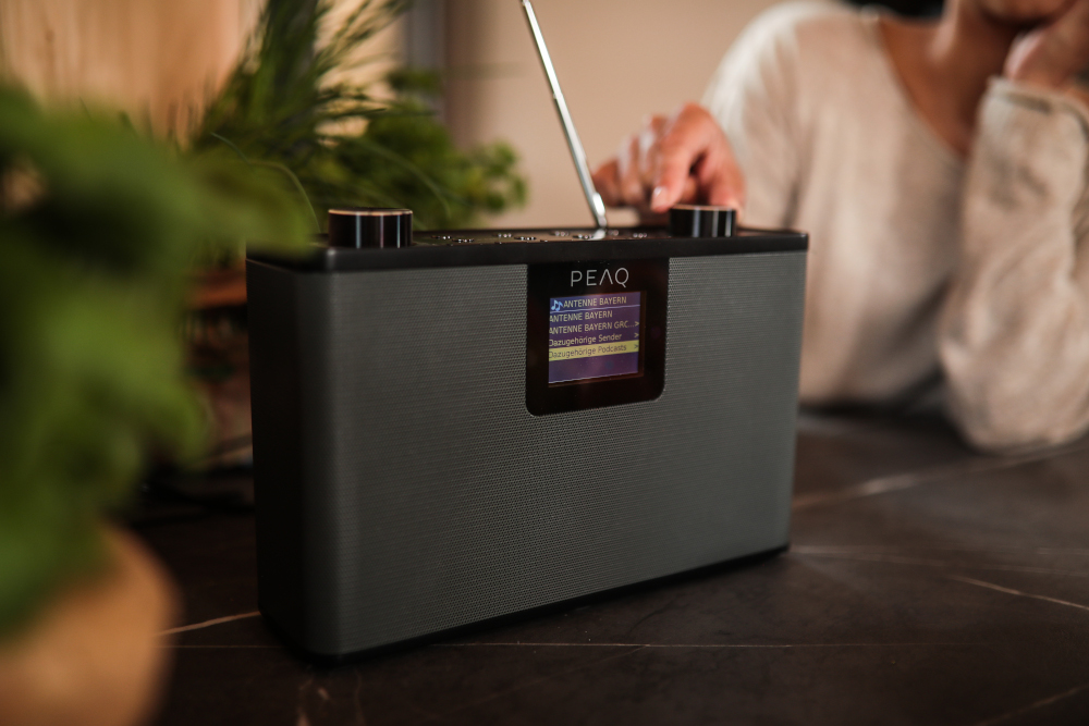 A person touches a black and grey radio with a small screen.