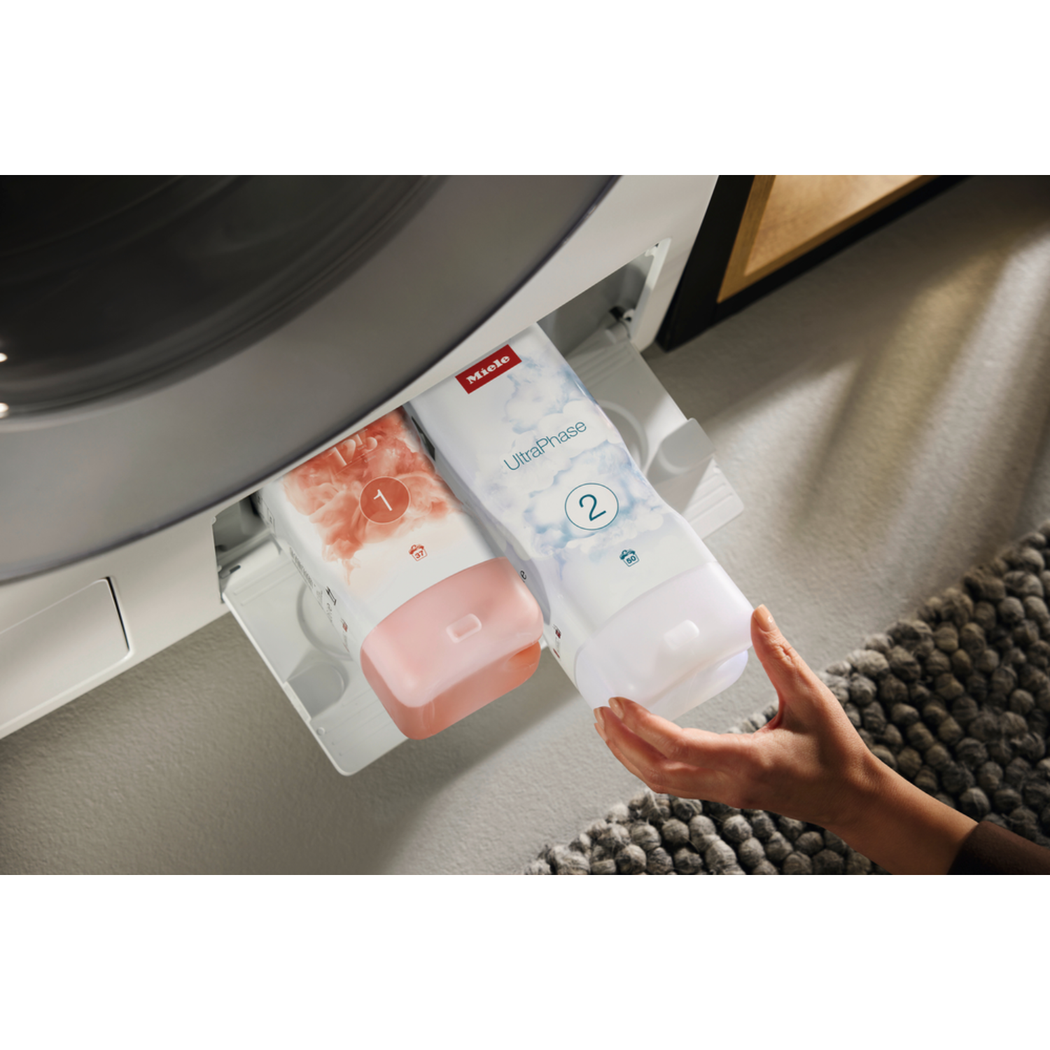 A washing machine drawer with two detergent pods being handled by a hand.