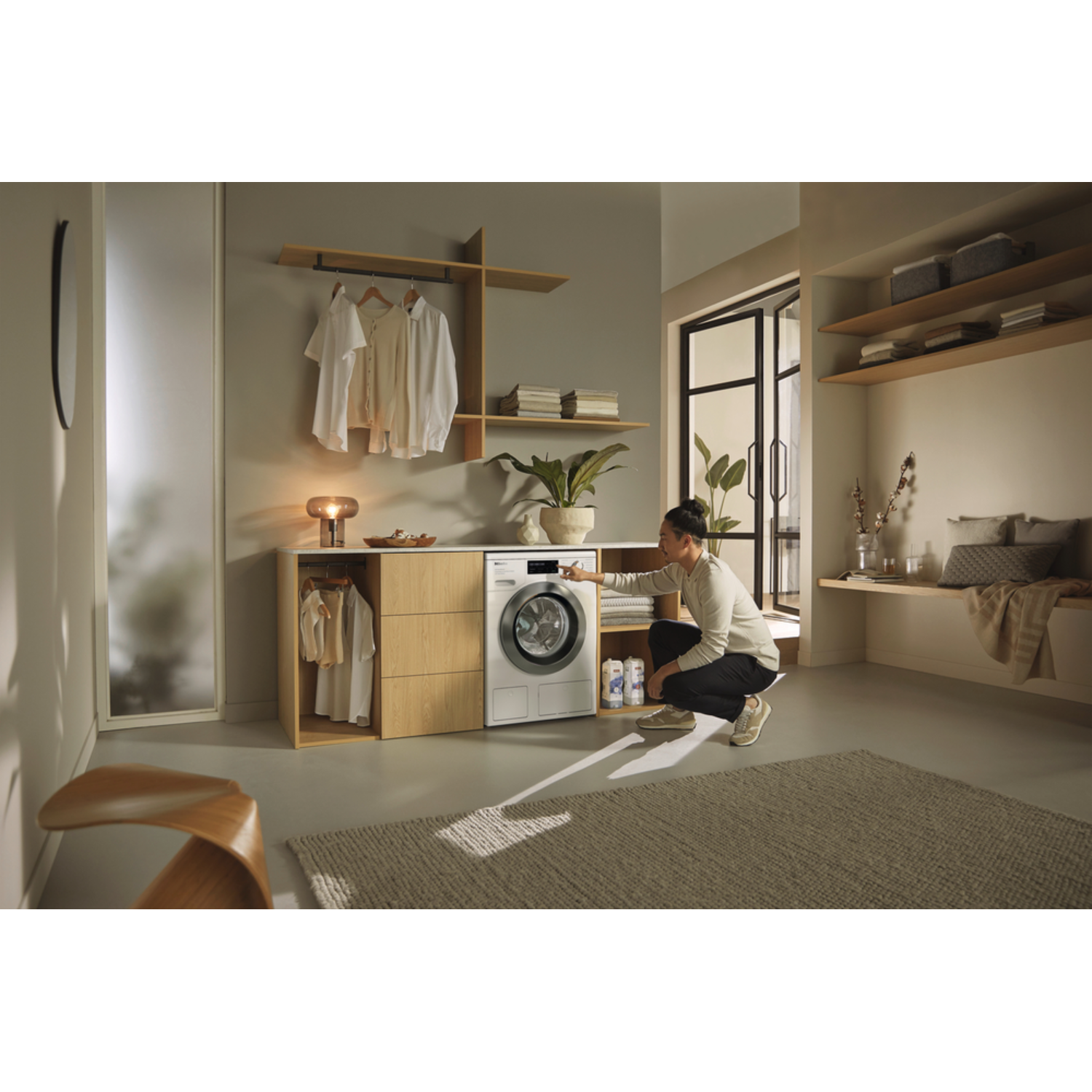 A person is in a modern room, using a washing machine. The room is white and gray with wood accents.