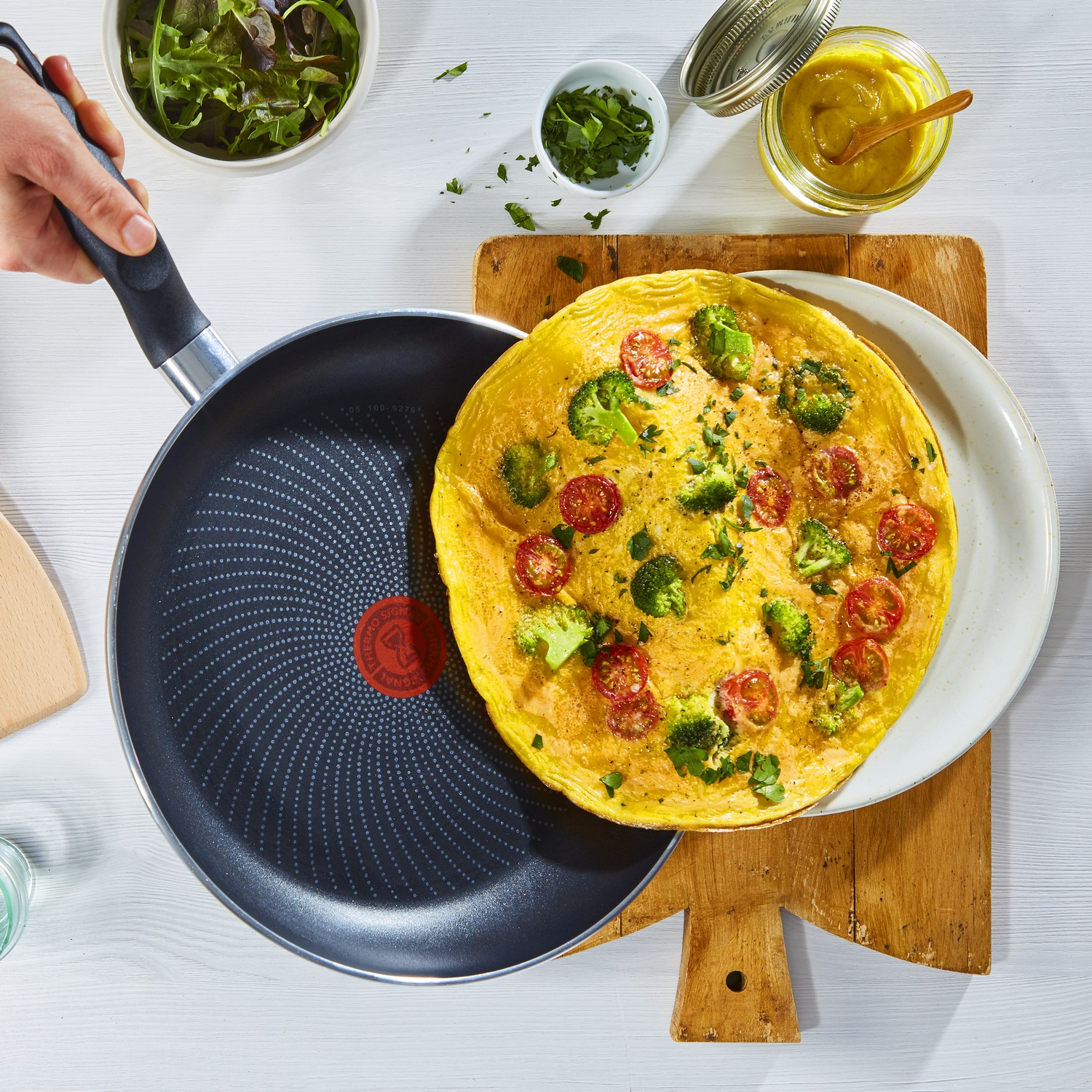 Omelet in een pan op een houten plank. Broccoli en tomaten zijn zichtbaar.