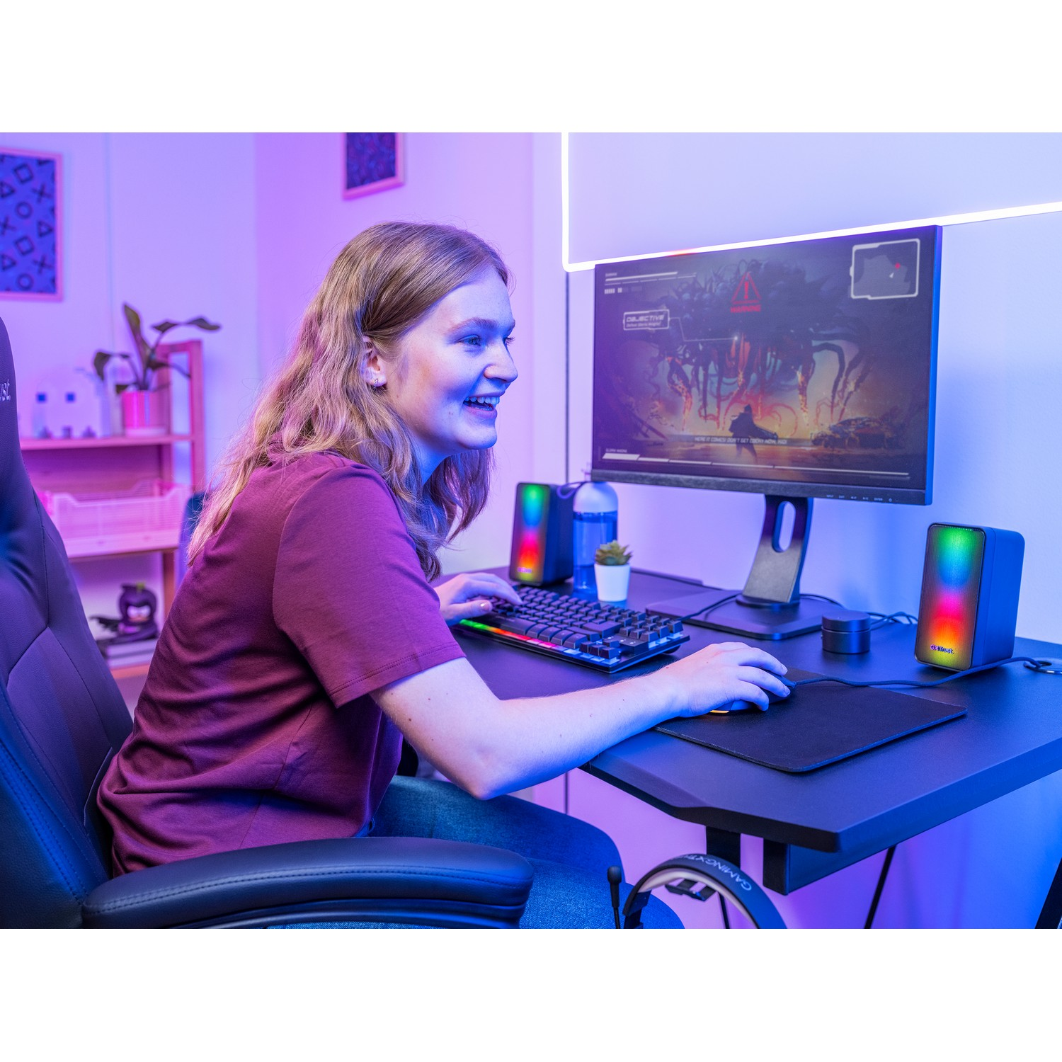 Jeune femme jouant avec un moniteur, des haut-parleurs, un clavier et une souris. Éclairage violet.