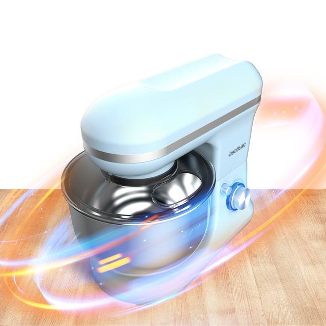 Batidora de pie azul claro con un cuenco de acero inoxidable, sobre una superficie de madera con destellos de luz naranja.