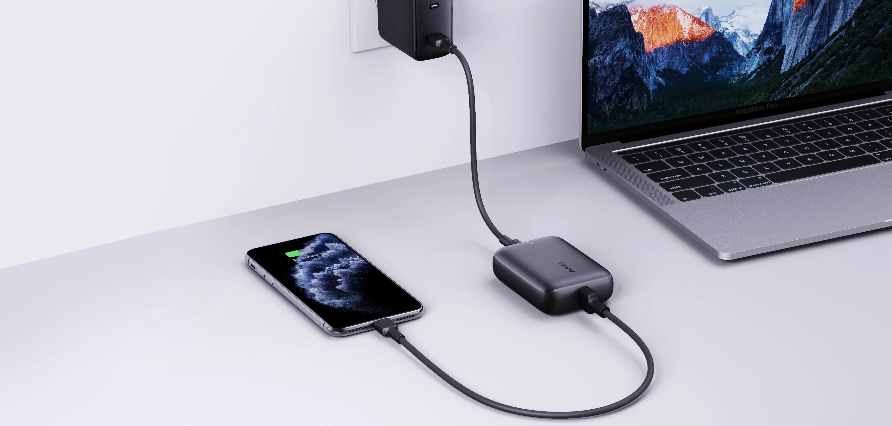 Un téléphone et un ordinateur portable sont en charge. Adaptateur secteur noir sur table blanche. Fond blanc.