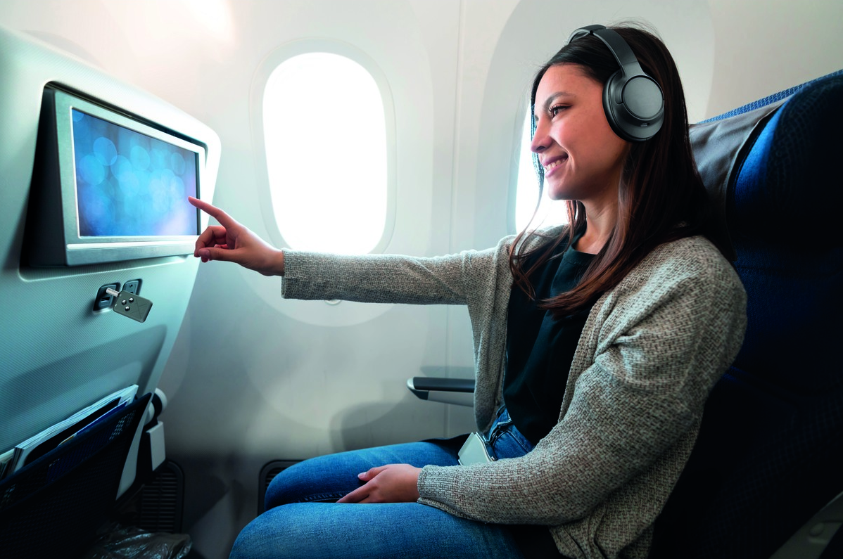 Une femme avec un casque touche un écran dans un avion.