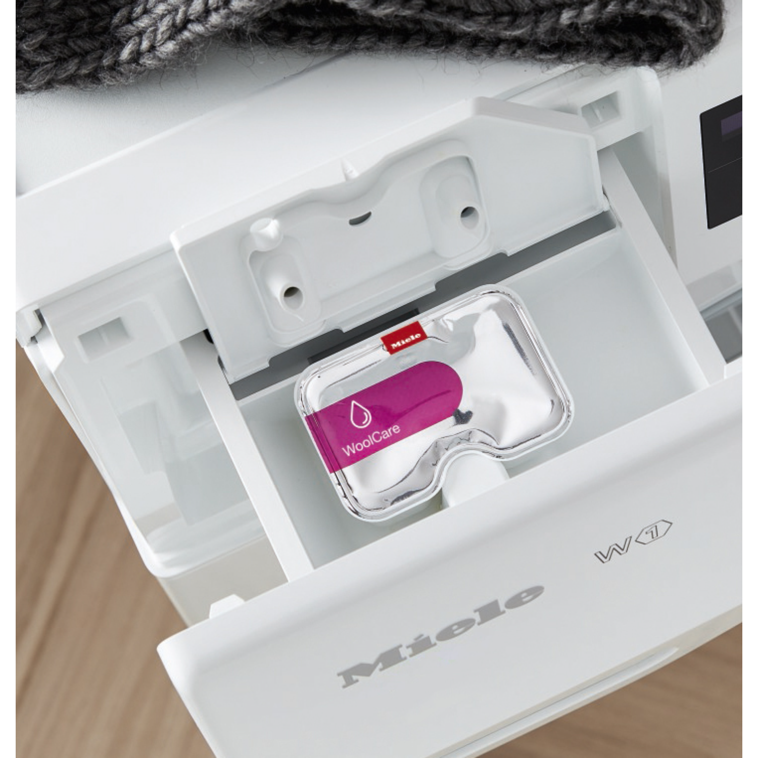 Washing machine drawer with a laundry detergent pack and a grey sweater.