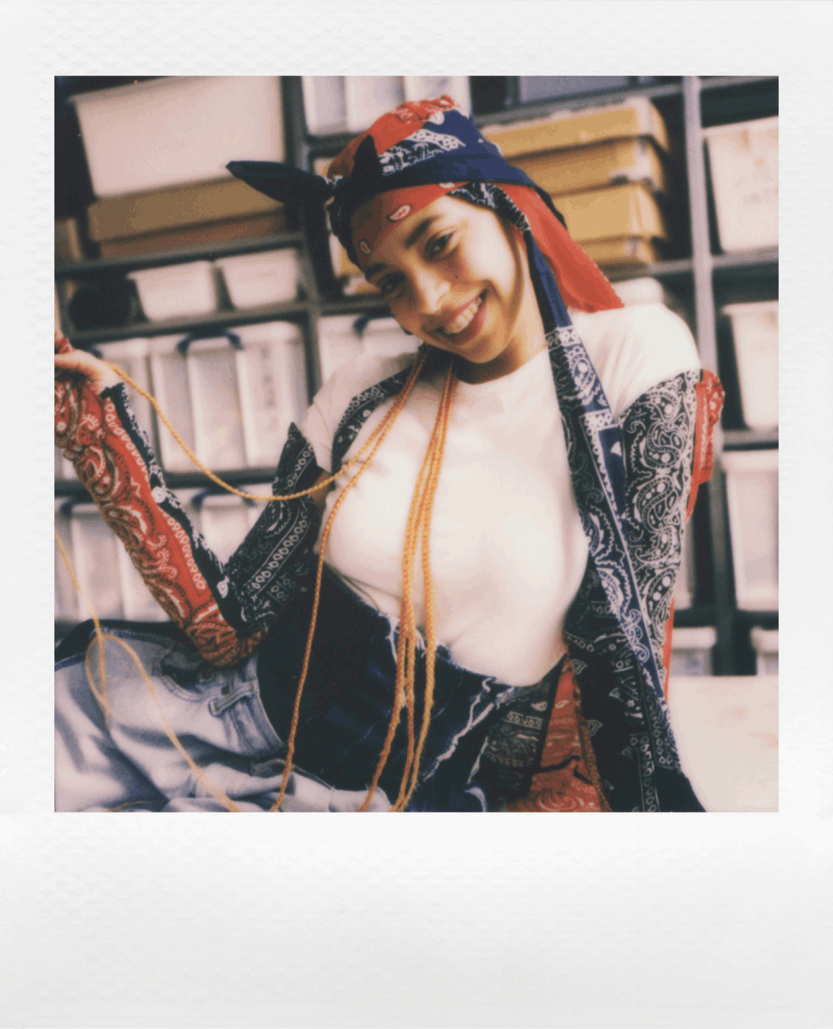 Una mujer con un atuendo colorido sonríe y sostiene una foto polaroid en una habitación.