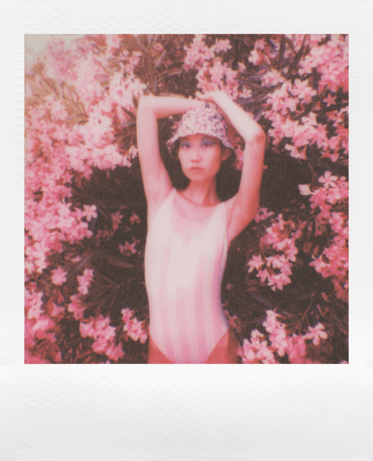 Mujer en traje de baño y sombrero rosas en arbusto de flores rosas. Estilo Polaroid.