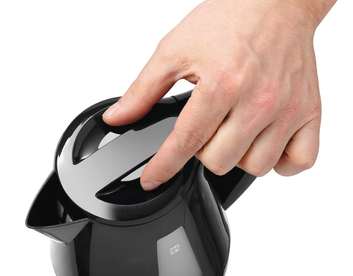 Die Hand einer Person drückt eine Taste auf einem schwarzen Wasserkocher. Der Wasserkocher steht auf weißem Untergrund.
