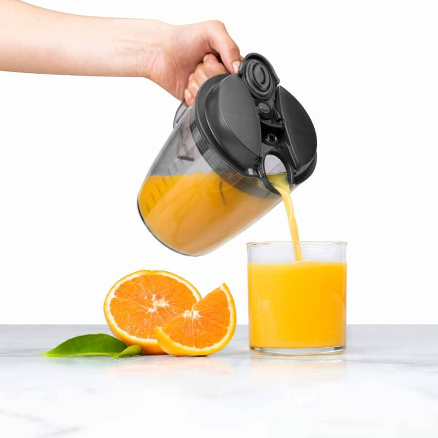 Kéz narancslét önt pohárba. Narancsszeletek az asztalon. Fehér háttér.