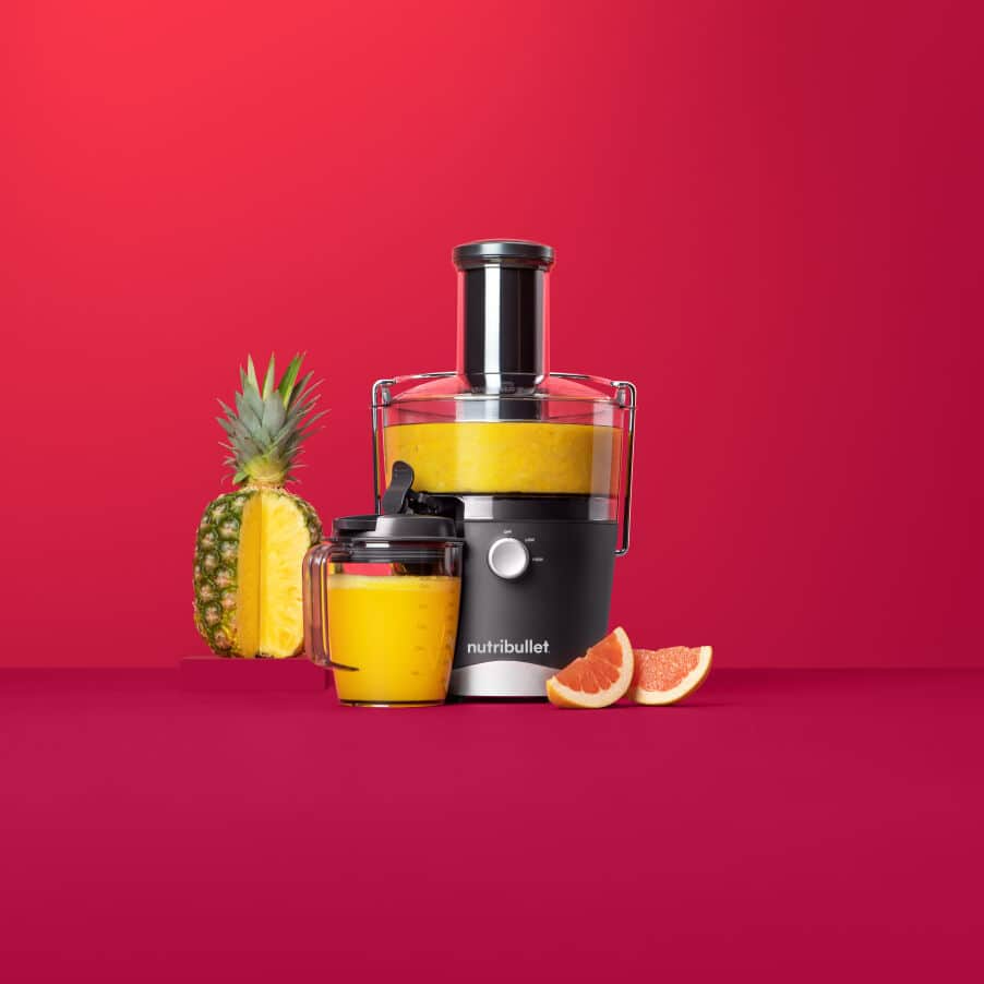 Gyümölcscentrifuga ananásszal, grapefruit-tal és lével. Piros háttér.