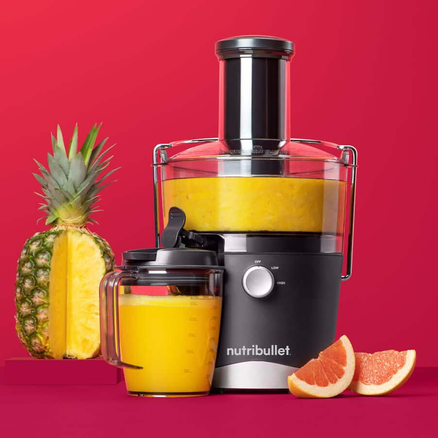 Egy gyümölcscentrifuga, ananász és grapefruit piros háttéren, egy pohár lével.