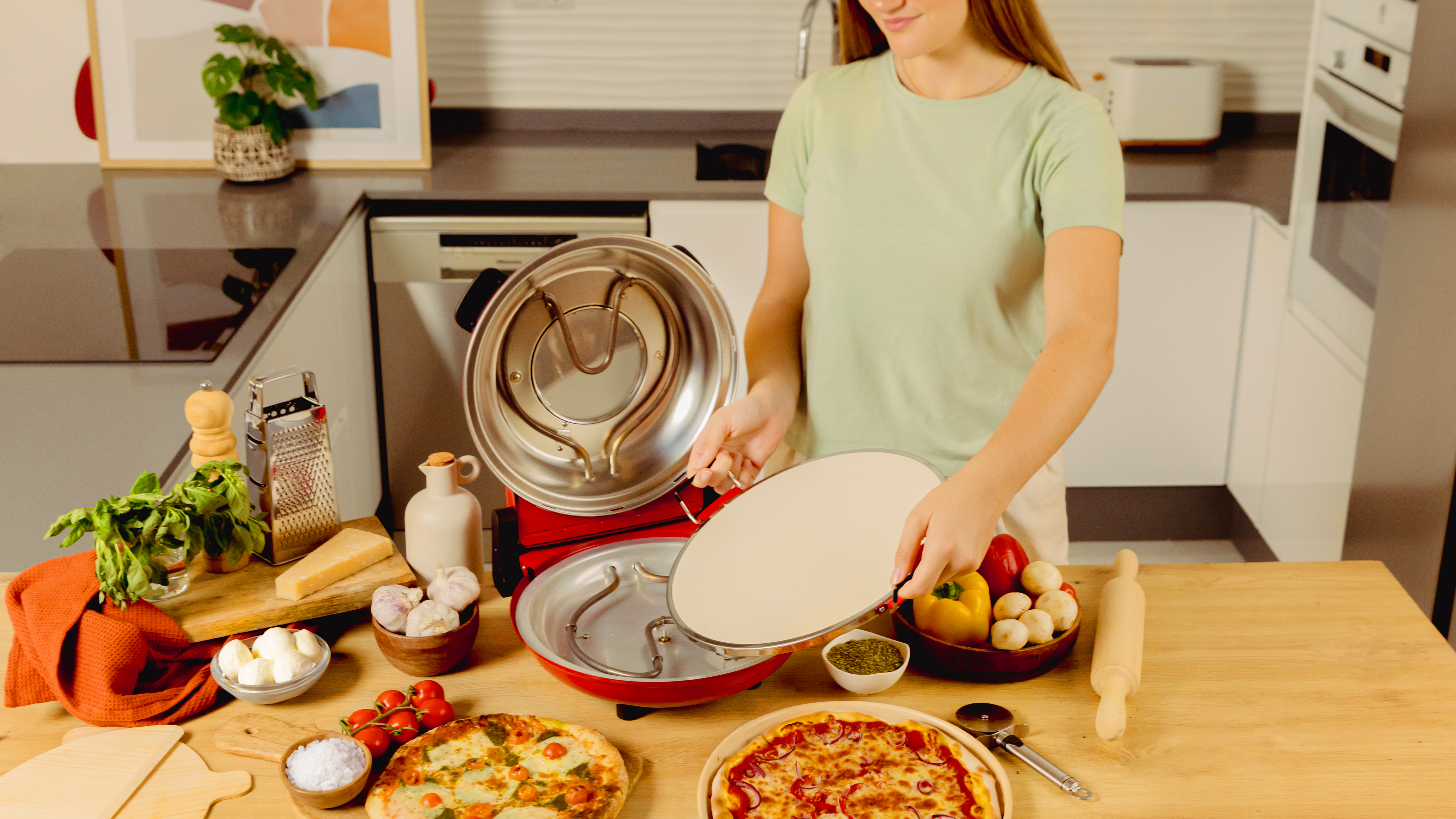 Una mujer sosteniendo una piedra para pizza, preparando una pizza con ingredientes en una encimera.