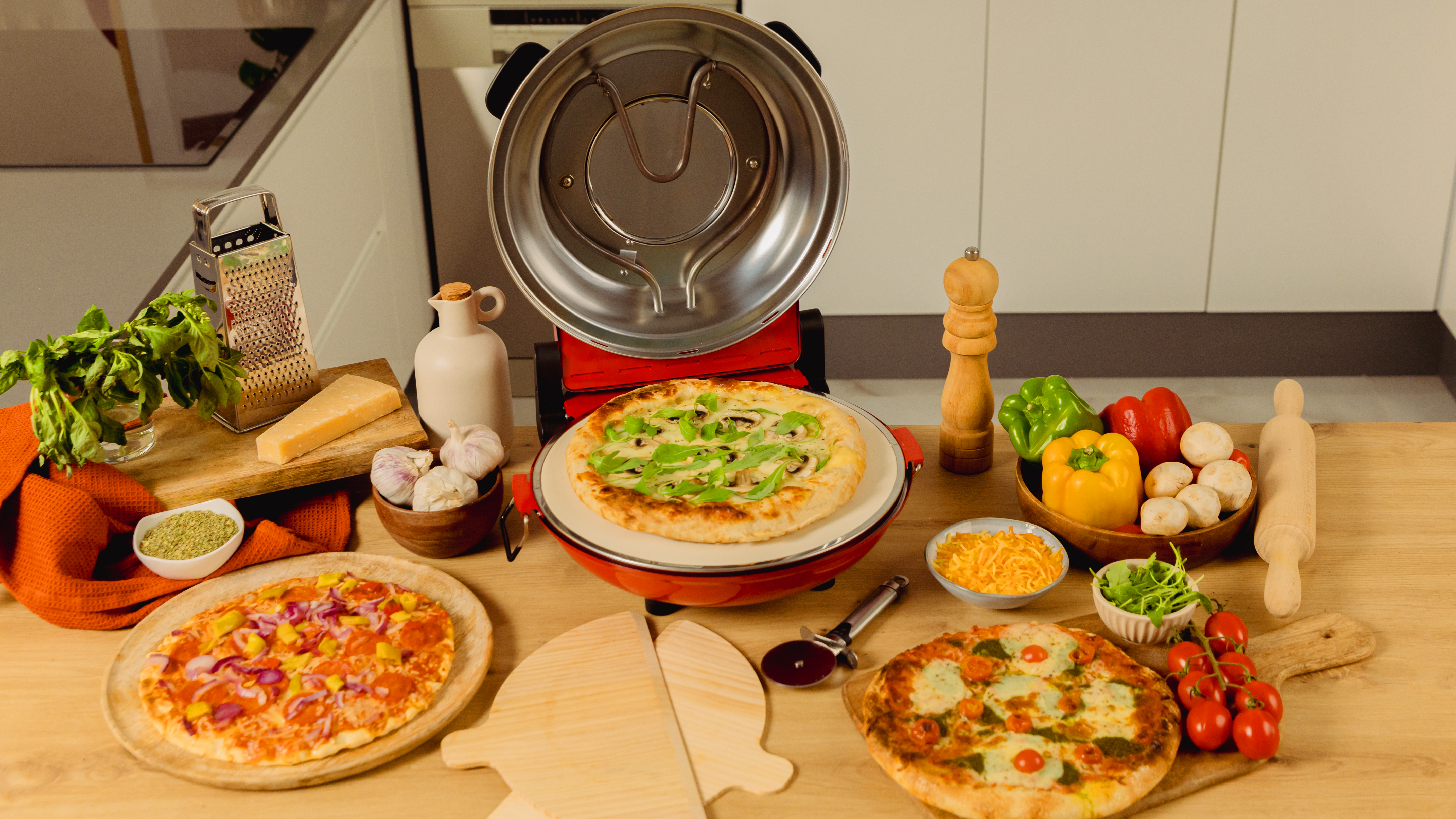 Pizza en piedra en horno rojo, rodeada de ingredientes en una mesa de madera.