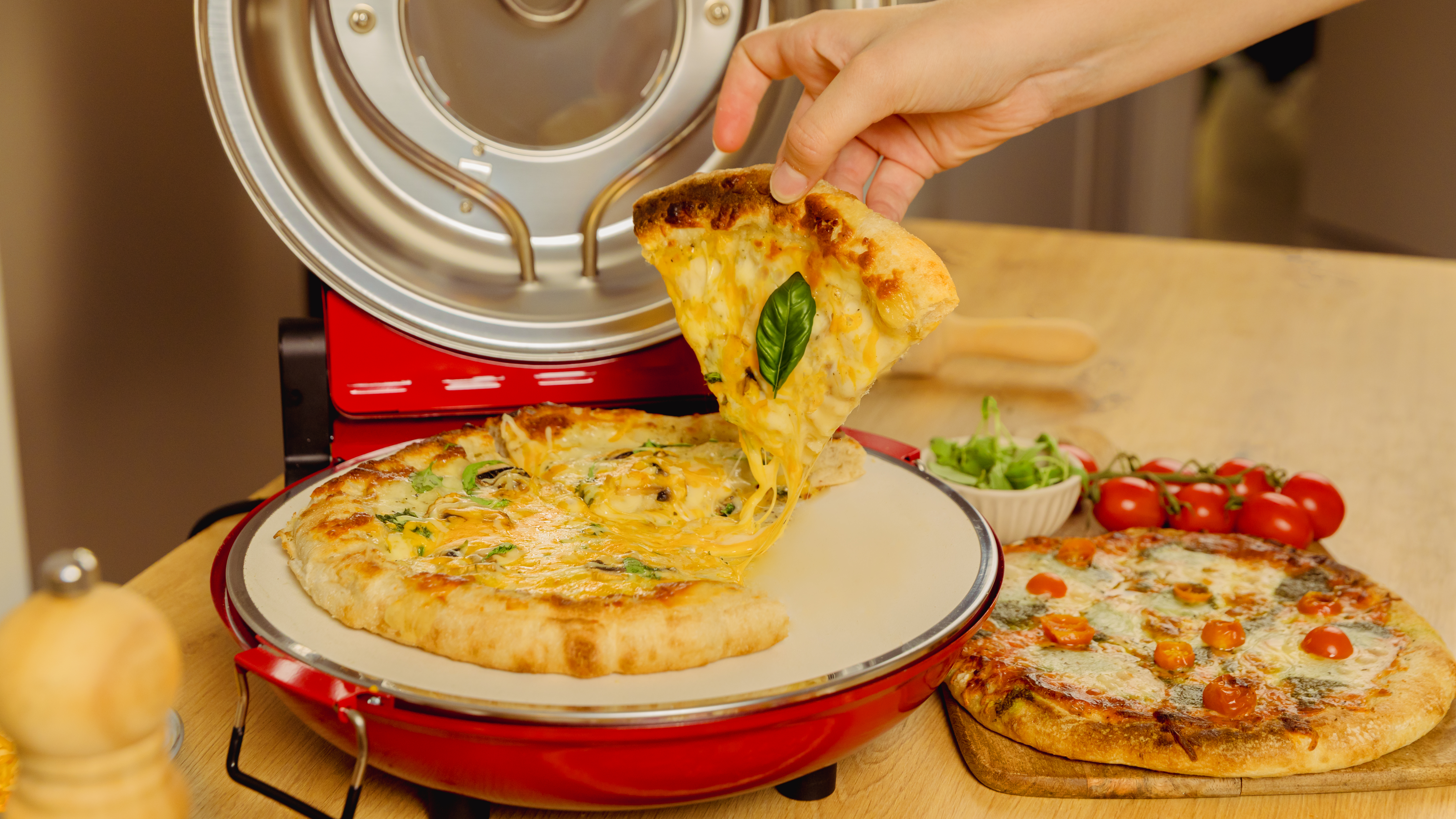 Una mano levanta una rebanada de pizza con queso fundido. Dos pizzas en un horno rojo.