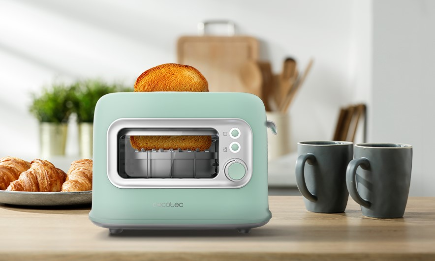 Tostadora verde menta con tostadas y dos tazas grises en una mesa de madera.