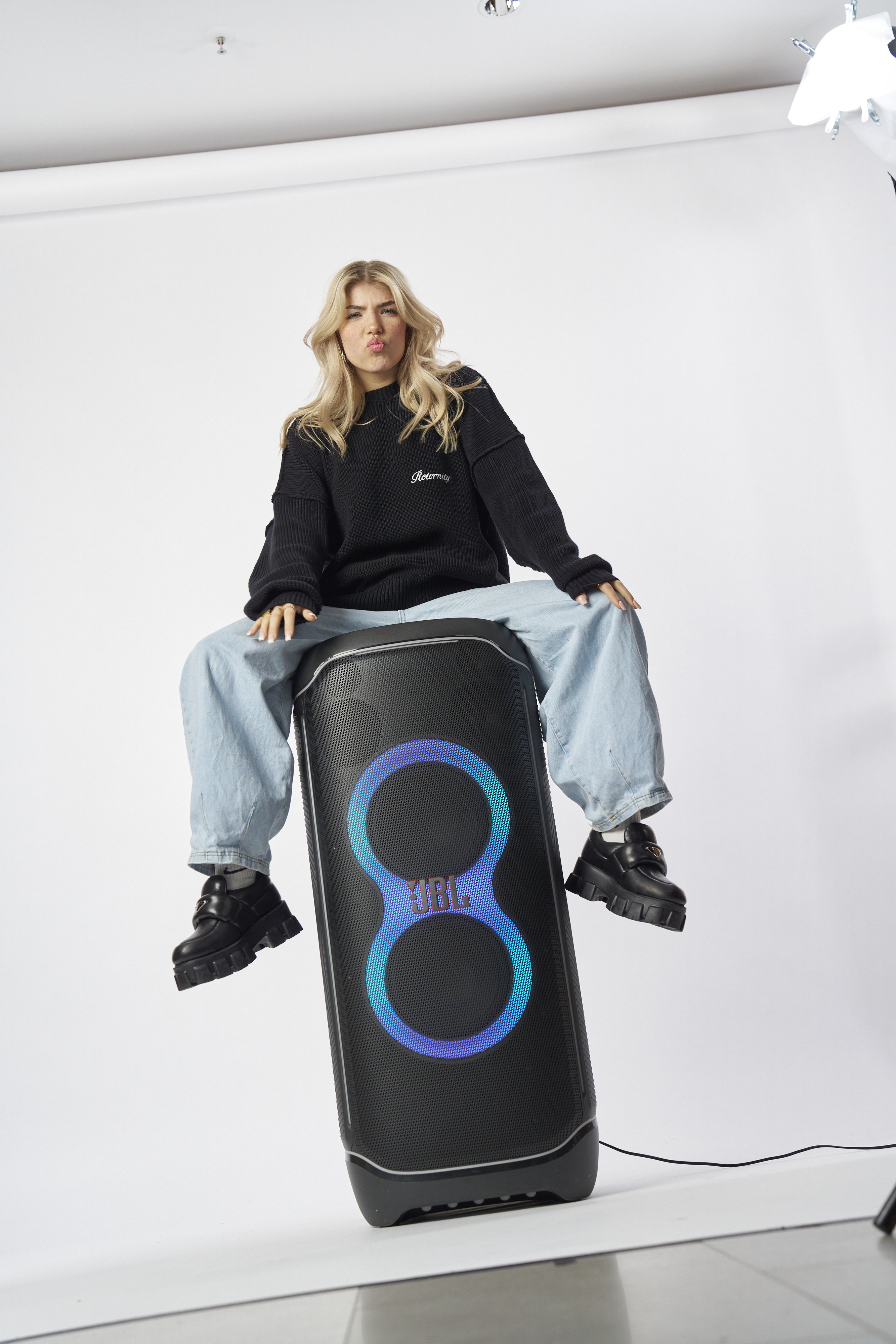 Eine blonde Frau sitzt auf einem JBL-Lautsprecher.
