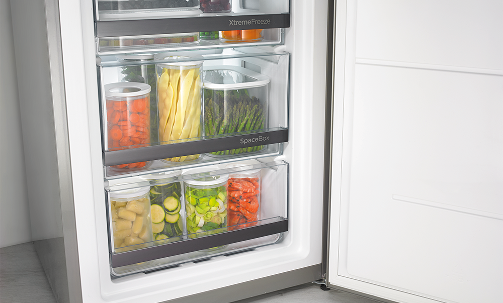 Wnętrze lodówki ze stosami przezroczystych pojemników z kolorowym, przygotowanym jedzeniem.