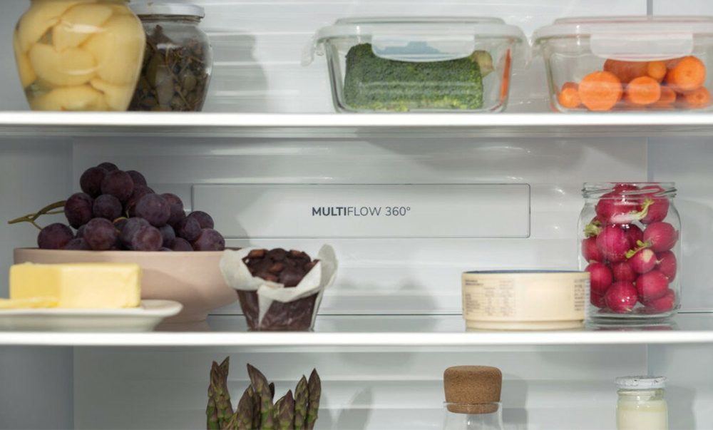 Wnętrze lodówki z półkami z jedzeniem: winogronami, masłem, babeczkami, rzodkiewkami. Białe wnętrze.