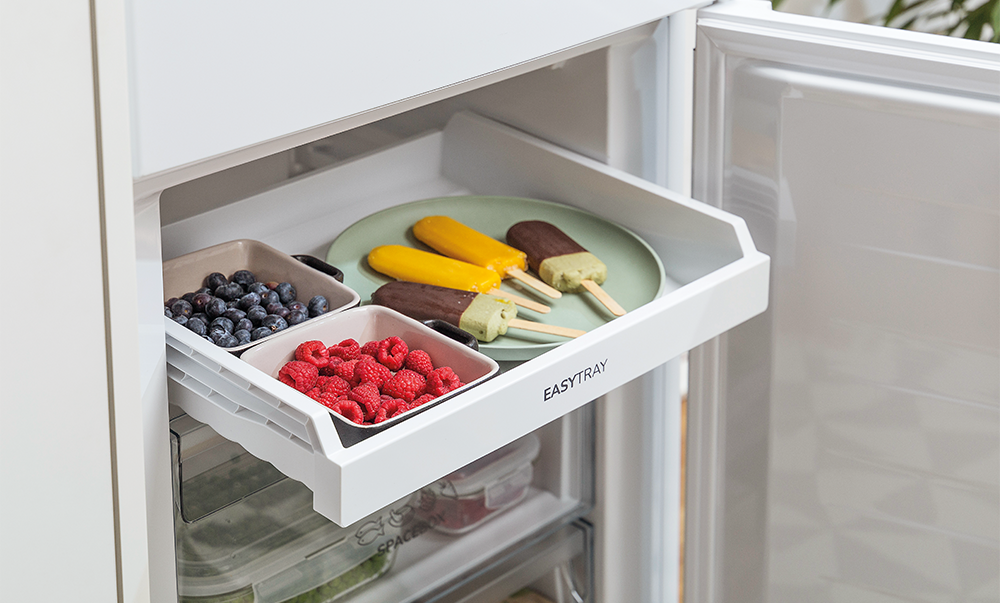 Szuflada lodówki z lodami, jagodami i talerzem. Biała lodówka.