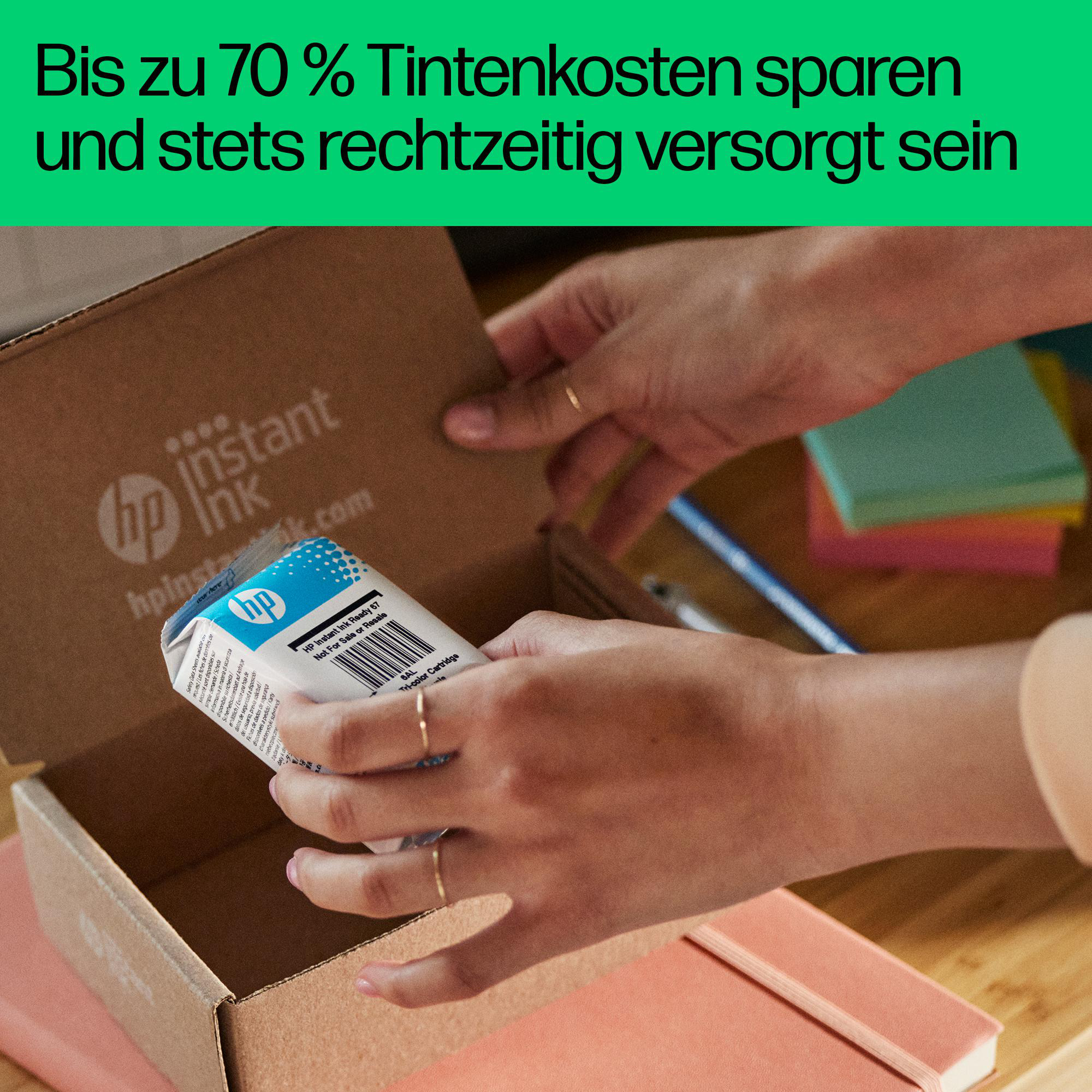 Hände öffnen einen Pappkarton mit HP Instant Ink Patronen und anderen Gegenständen auf dem Tisch.