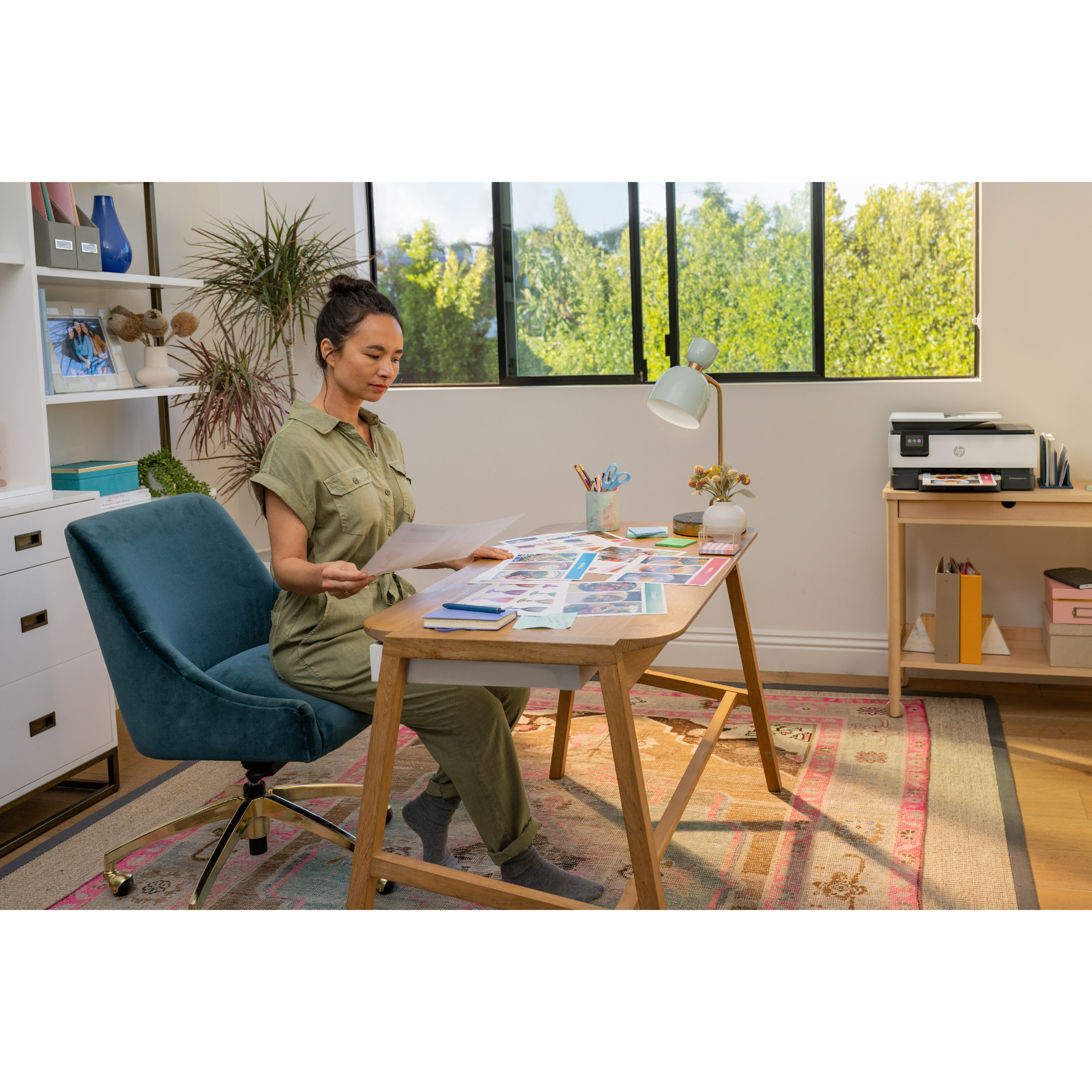 A woman working at a desk with a printer, computer, and other office supplies.