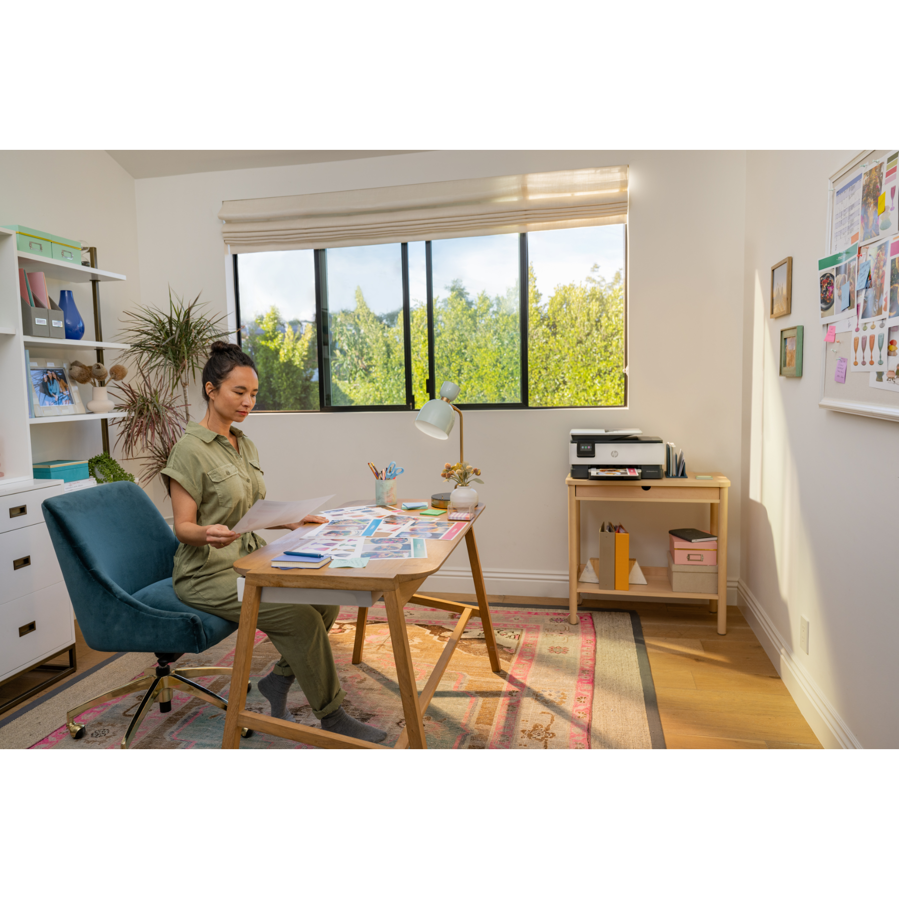 Vrouw aan bureau, papieren vasthoudend, werkend in thuiskantoor. Raam en printer zichtbaar. Groene bomen buiten.