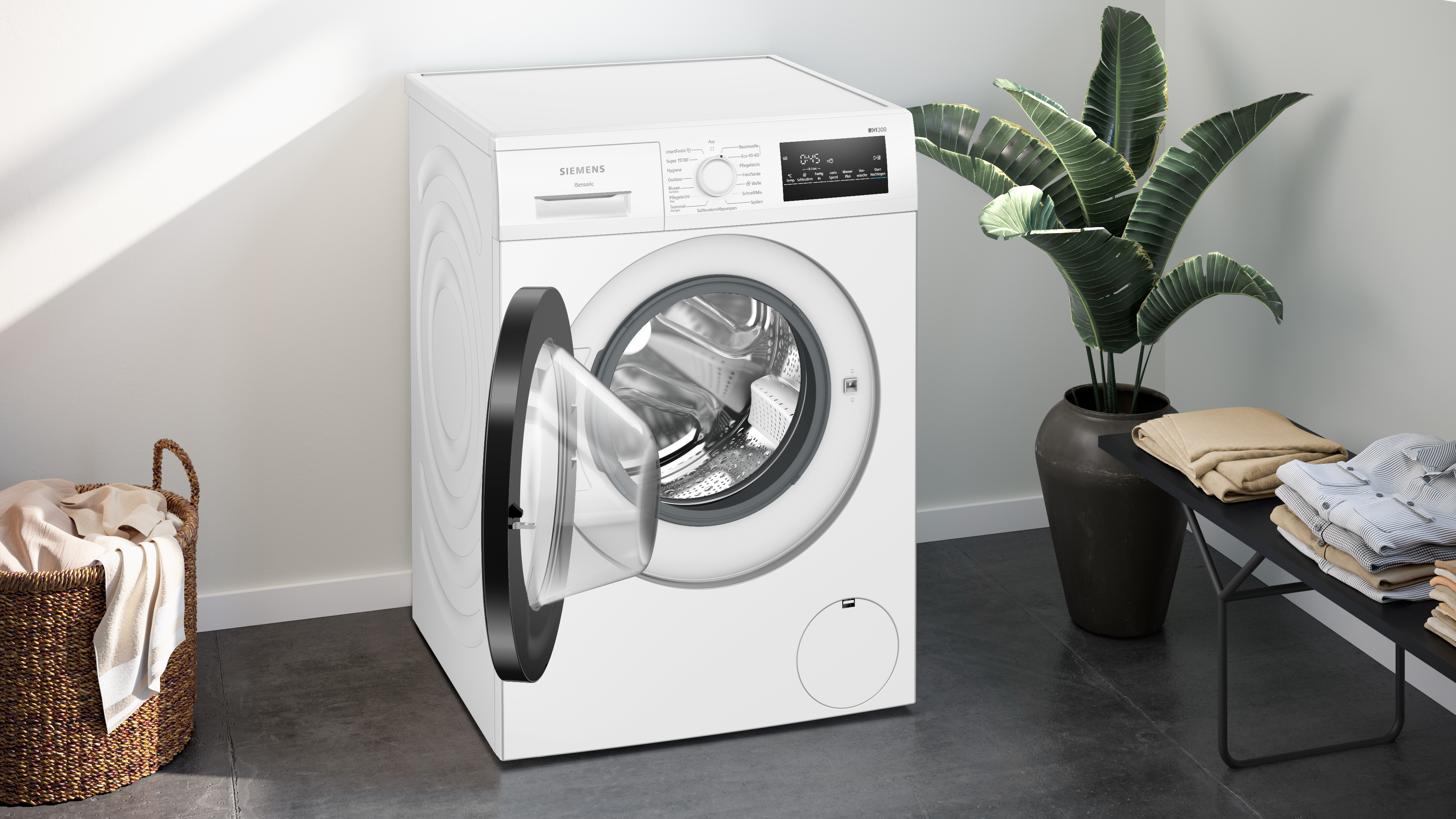 Eine weiße Siemens Waschmaschine mit geöffneter Tür. Ein Wäschekorb und Kleidung befinden sich in der Nähe.