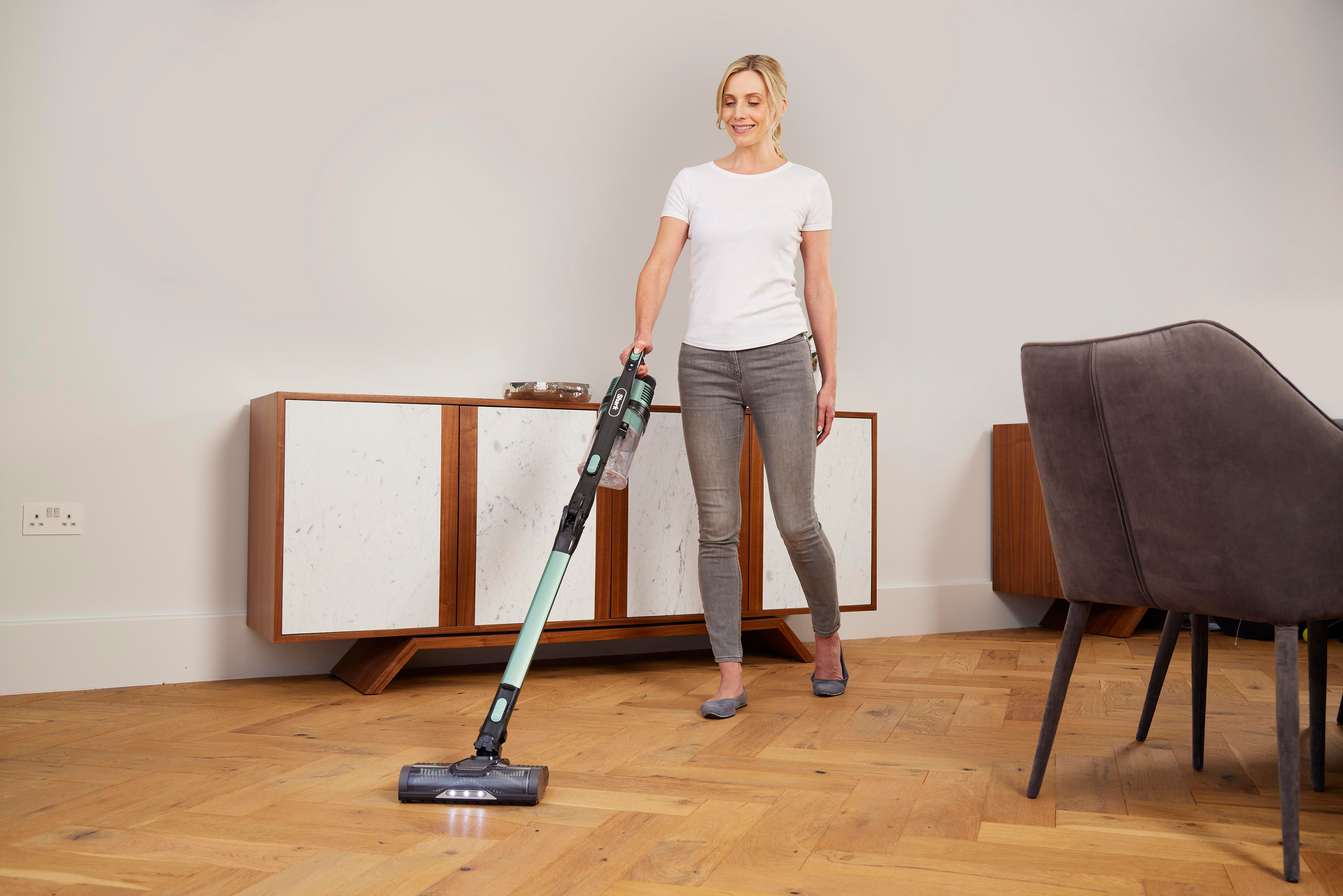 Frau geht, saugt Holzboden mit einem mintgrünen Staubsauger.