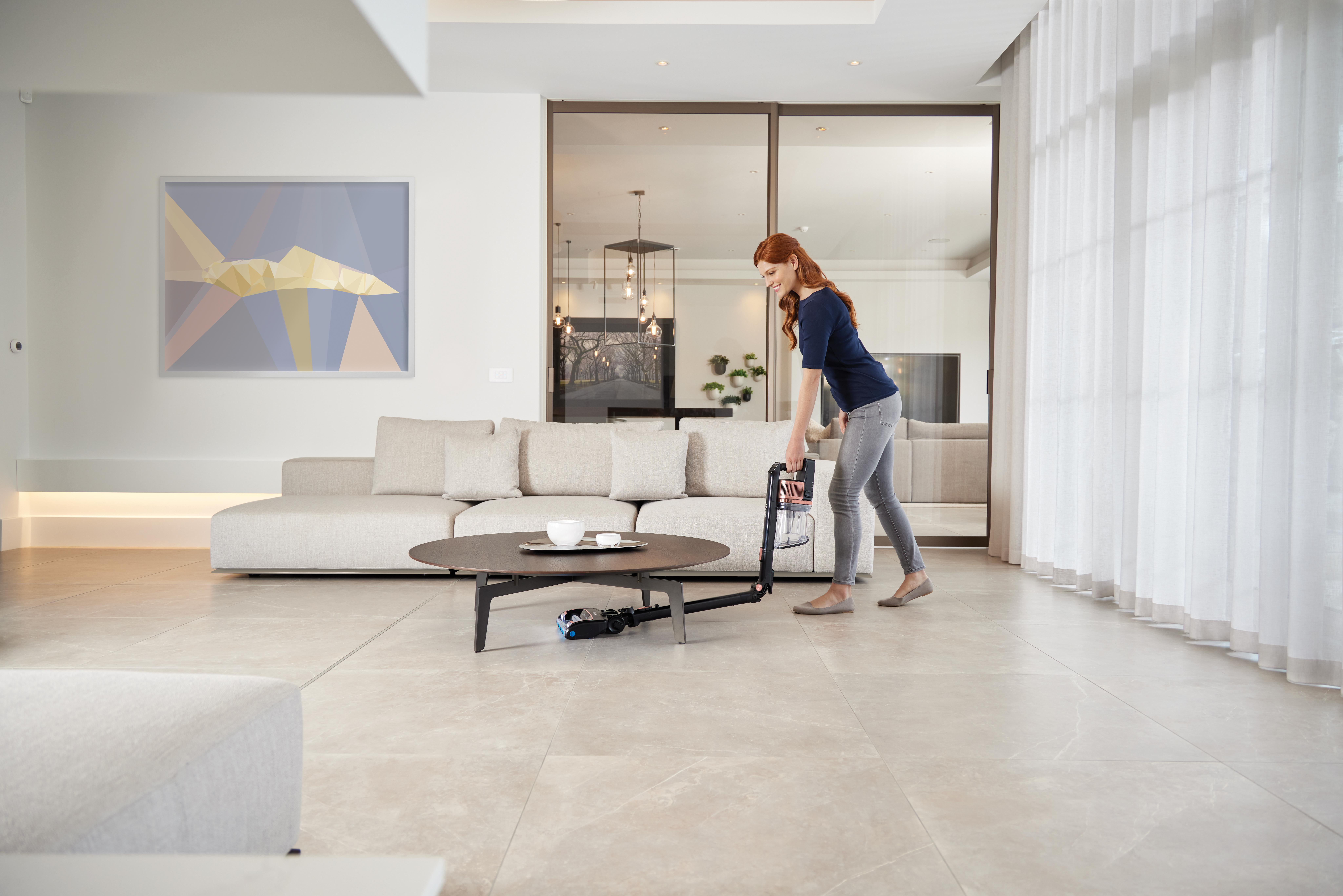 Frau, die ein Wohnzimmer mit Sofa, rundem Tisch und Gemälde saugt.