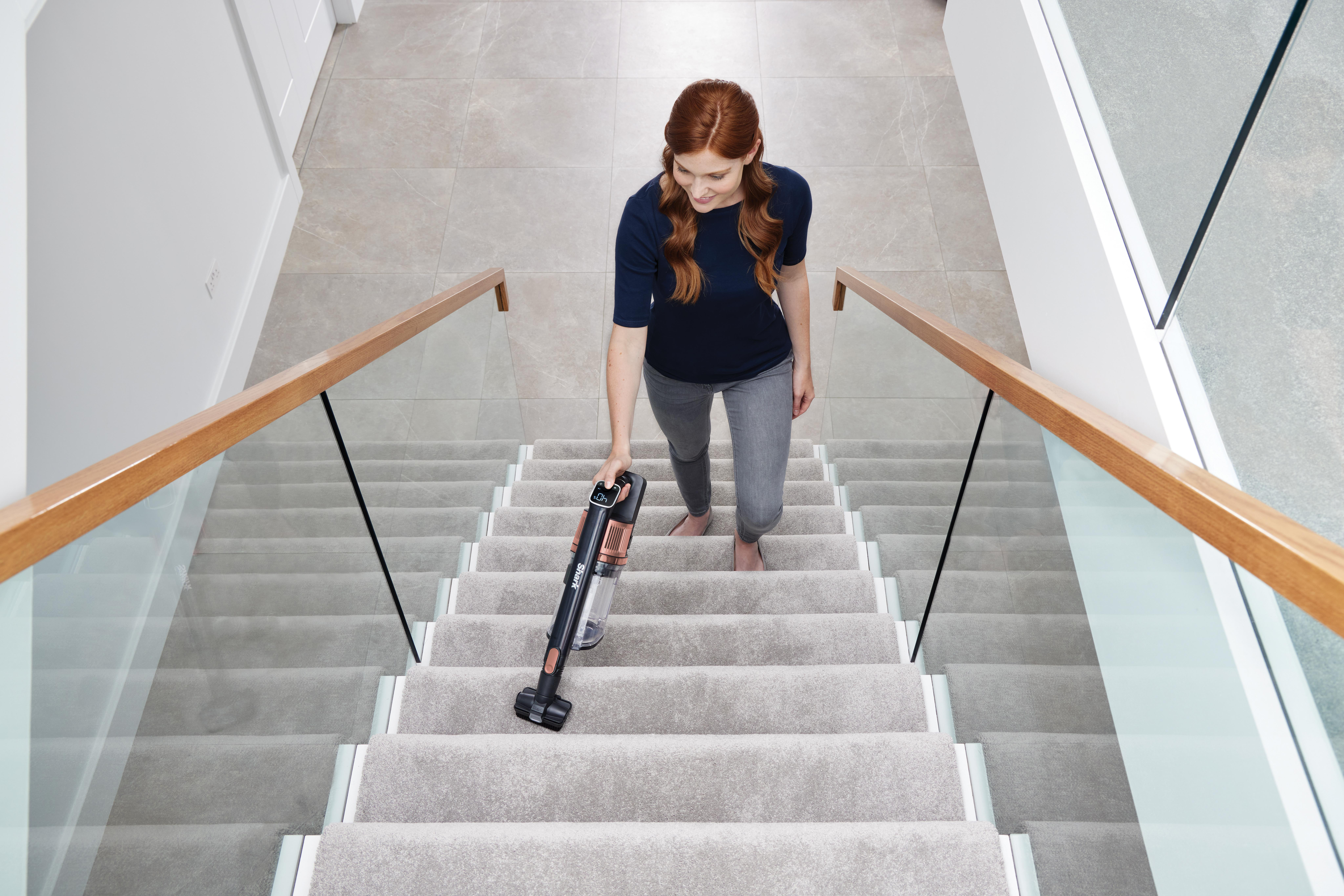 Frau, die Treppen mit einem Handstaubsauger saugt, aus der Vogelperspektive.