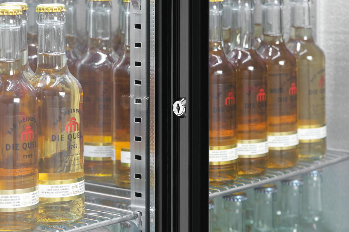Flaschen mit Die Quelle-Getränken werden in einem Kühlschrank ausgestellt. Die Tür ist geschlossen, ein Schloss ist sichtbar. Die Flaschen stehen auf Regalen.