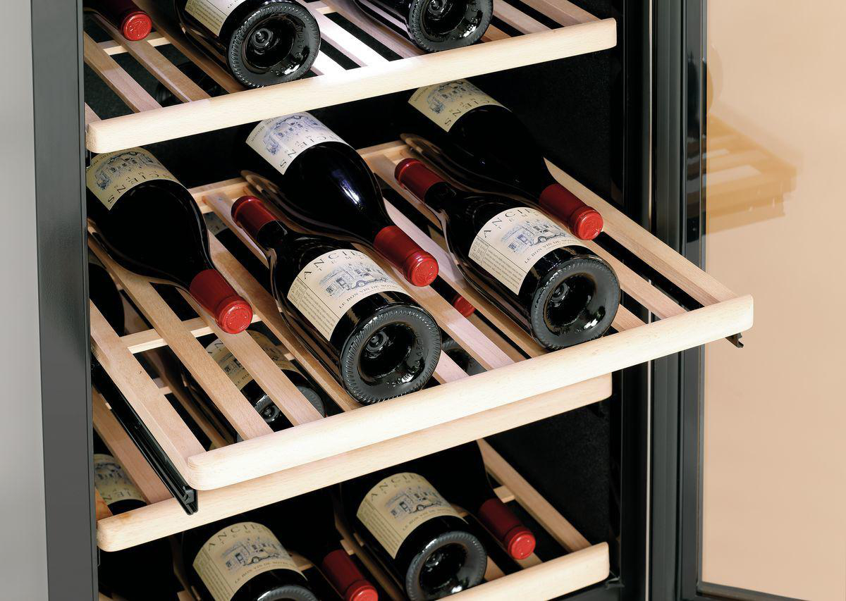 Wein wird in einem Holzweinregal gelagert. Die Flaschen sind meist schwarz mit roten Kappen und weißen Etiketten.
