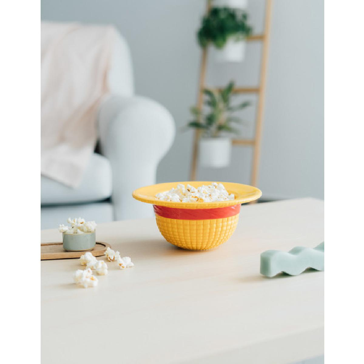 Gelbe Popcornschüssel auf einem hellen Tisch, Popcorn verstreut.