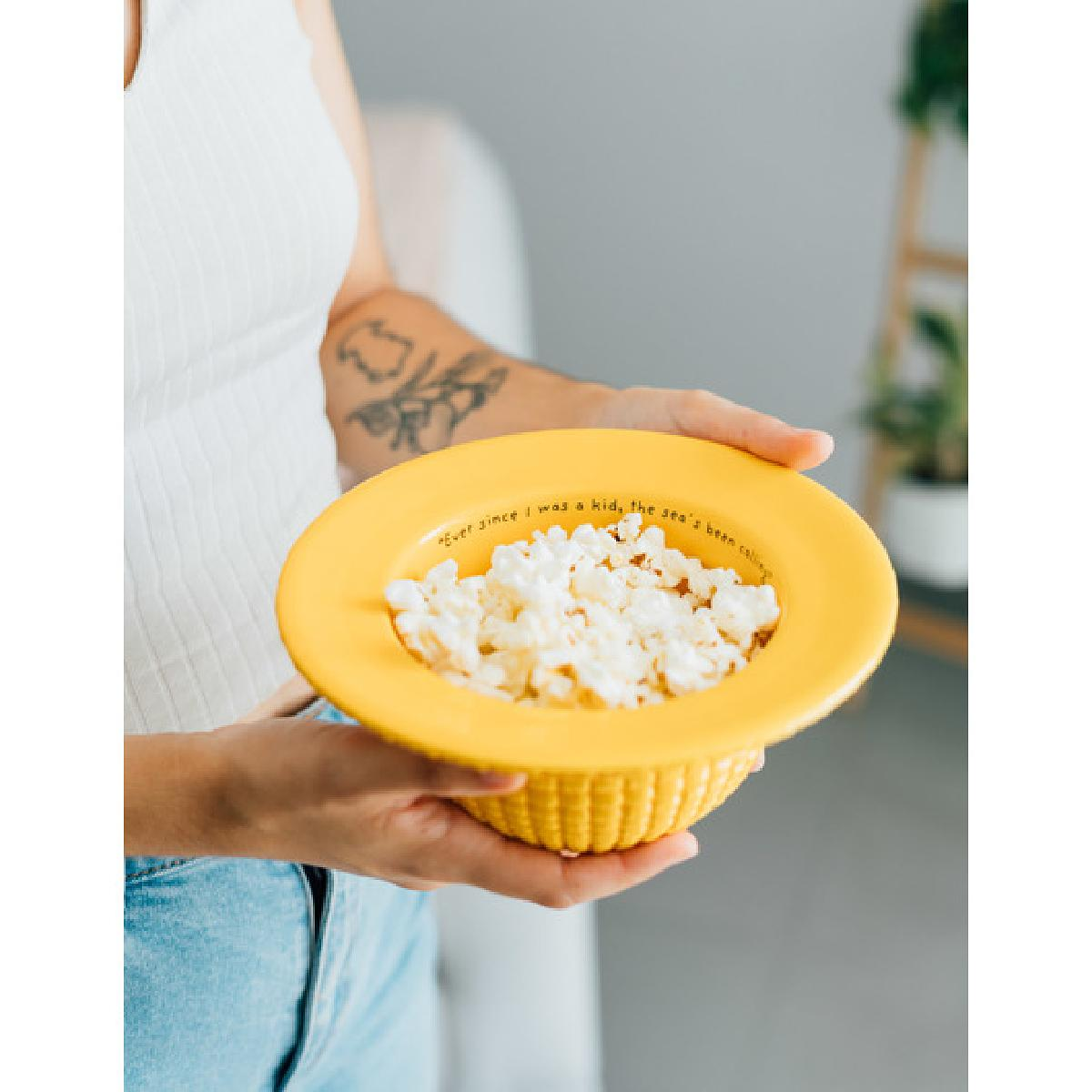 Person hält eine gelbe Schüssel mit Popcorn. Die Schüssel hat Text am Rand.
