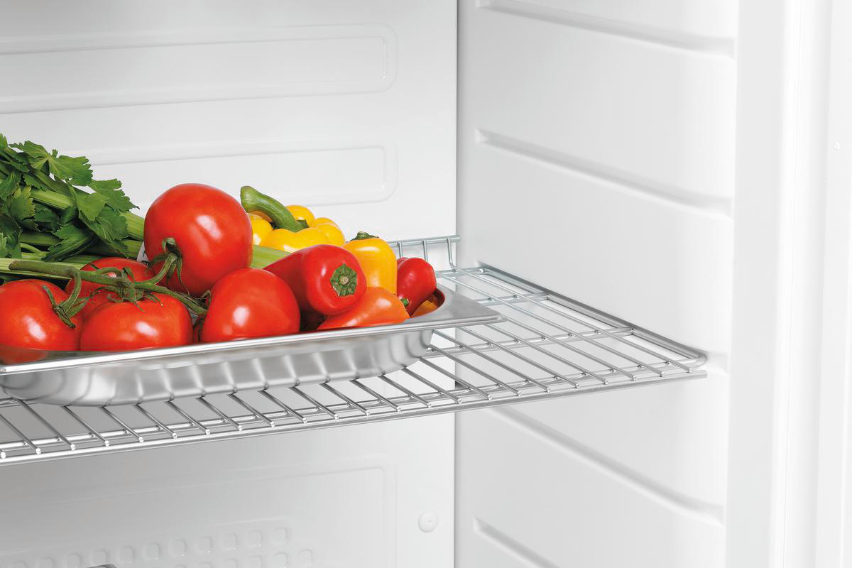 Im Kühlschrank liegen Tomaten, gelbe Paprika und Sellerie auf einem Metalltablett. Der Kühlschrank ist weiß.