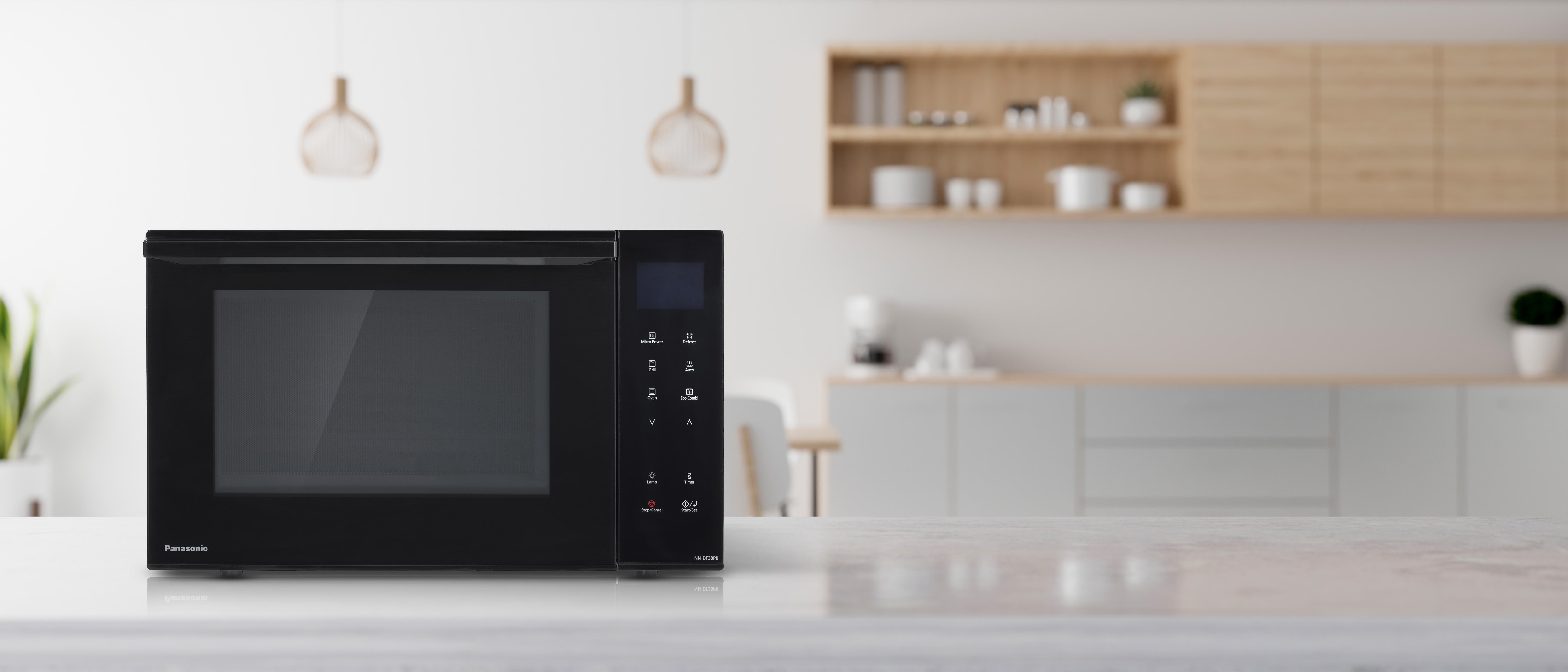 Schwarze Panasonic Mikrowelle auf einer weißen Theke, mit Küche im Hintergrund.