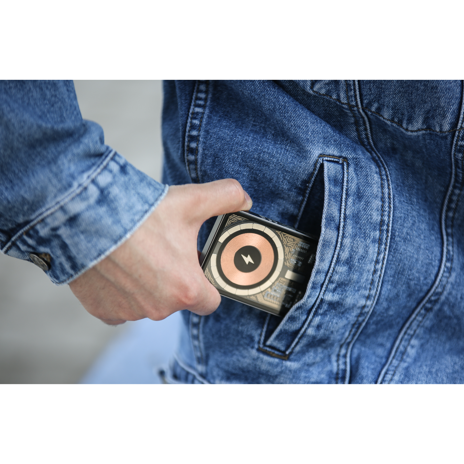 Hand die een draadloze oplader in een jeanszak houdt. Oplader is zwart met een koperkleurige cirkel.