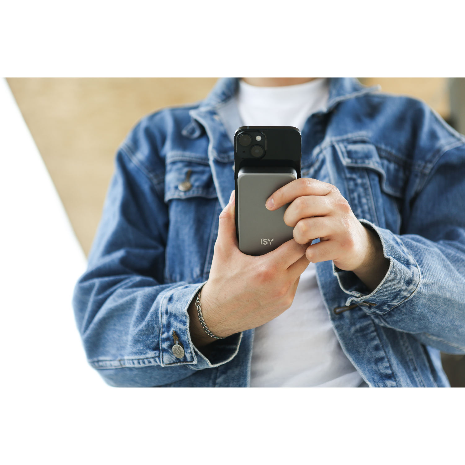 Man houdt telefoon vast met grijze oplader; draagt spijkerjas. Achtergrond is wazig.