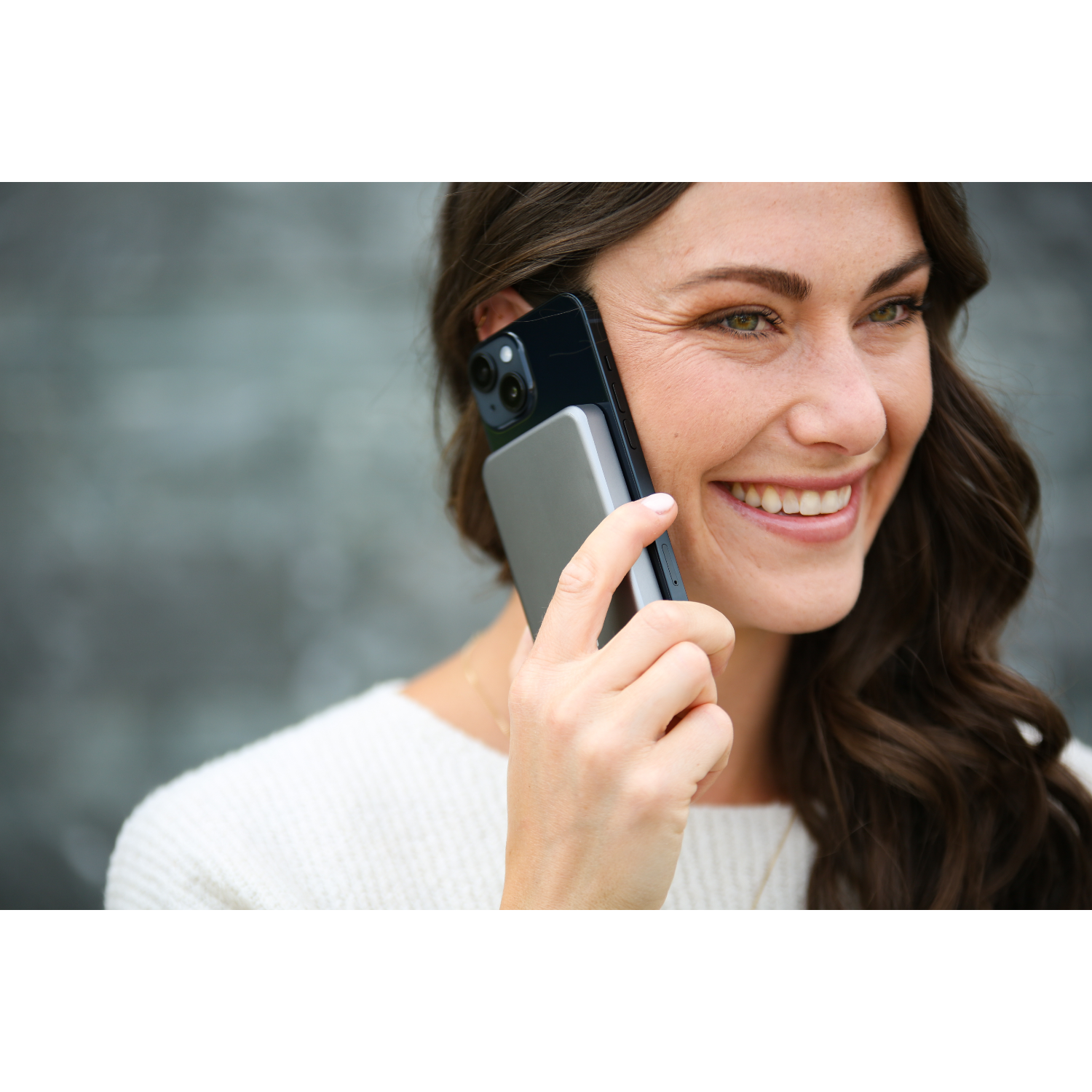 Woman smiling while holding a phone and a power bank to her ear.