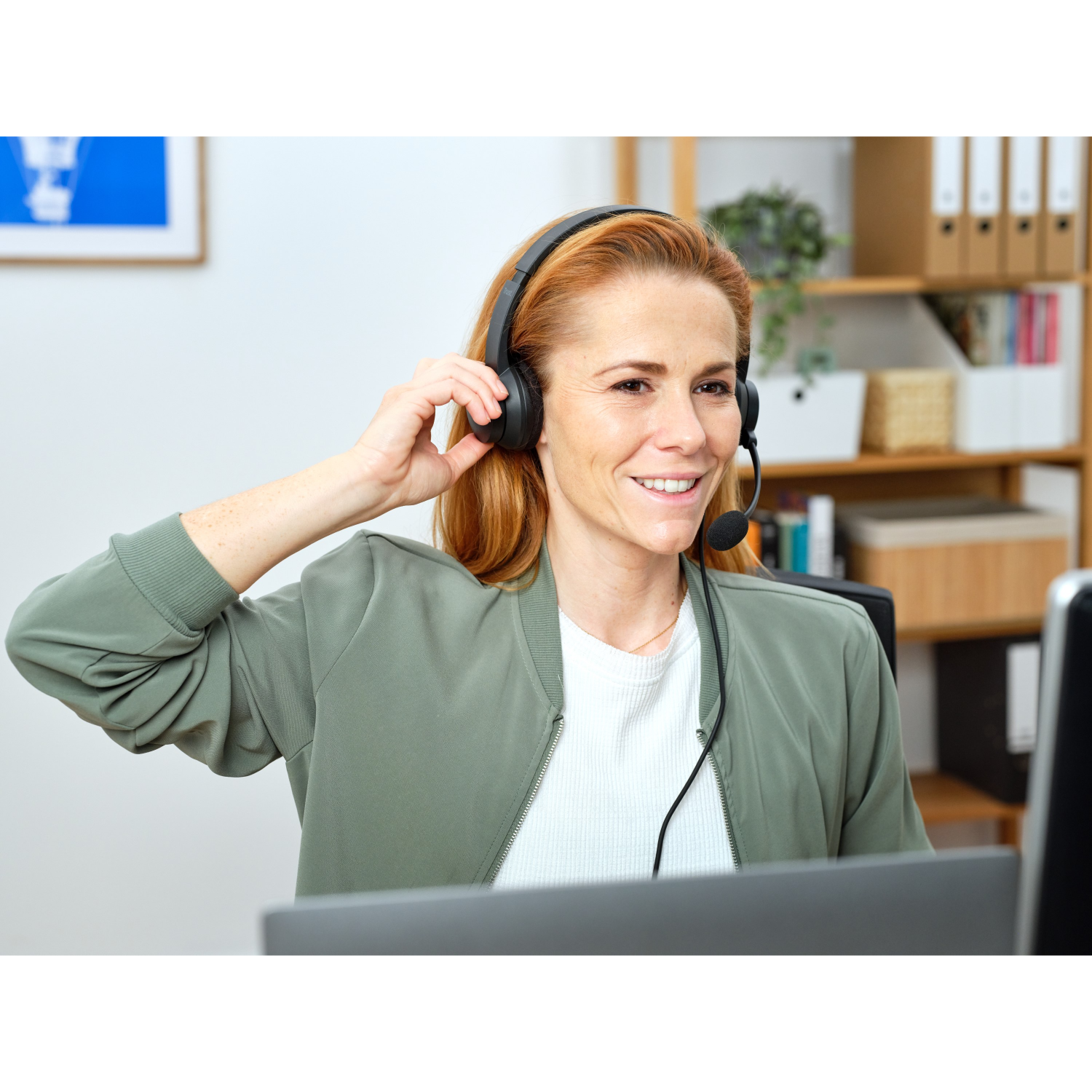 Woman with red hair wearing a headset, smiling, working on a laptop.
