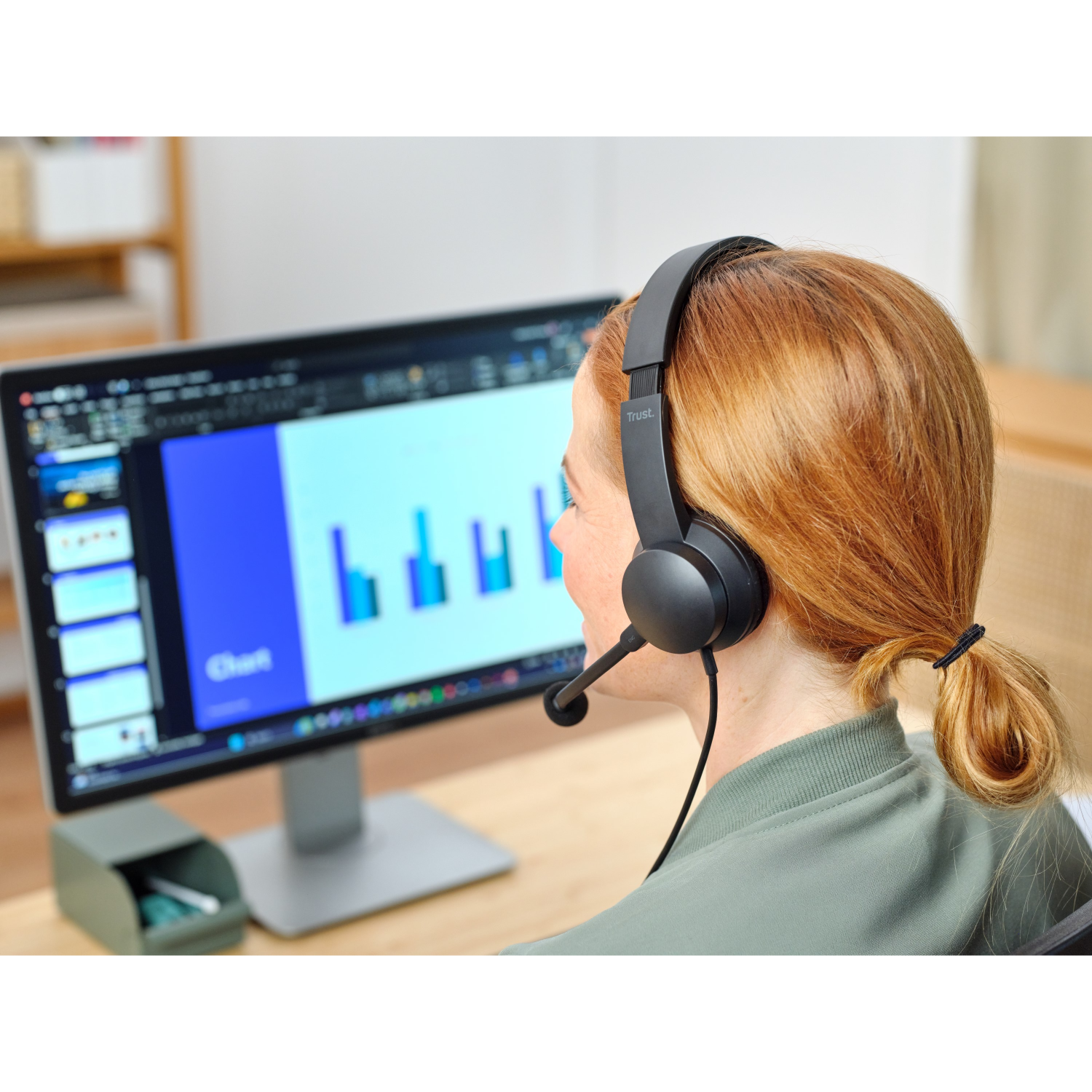Woman with red hair wearing a headset, looking at a computer screen.