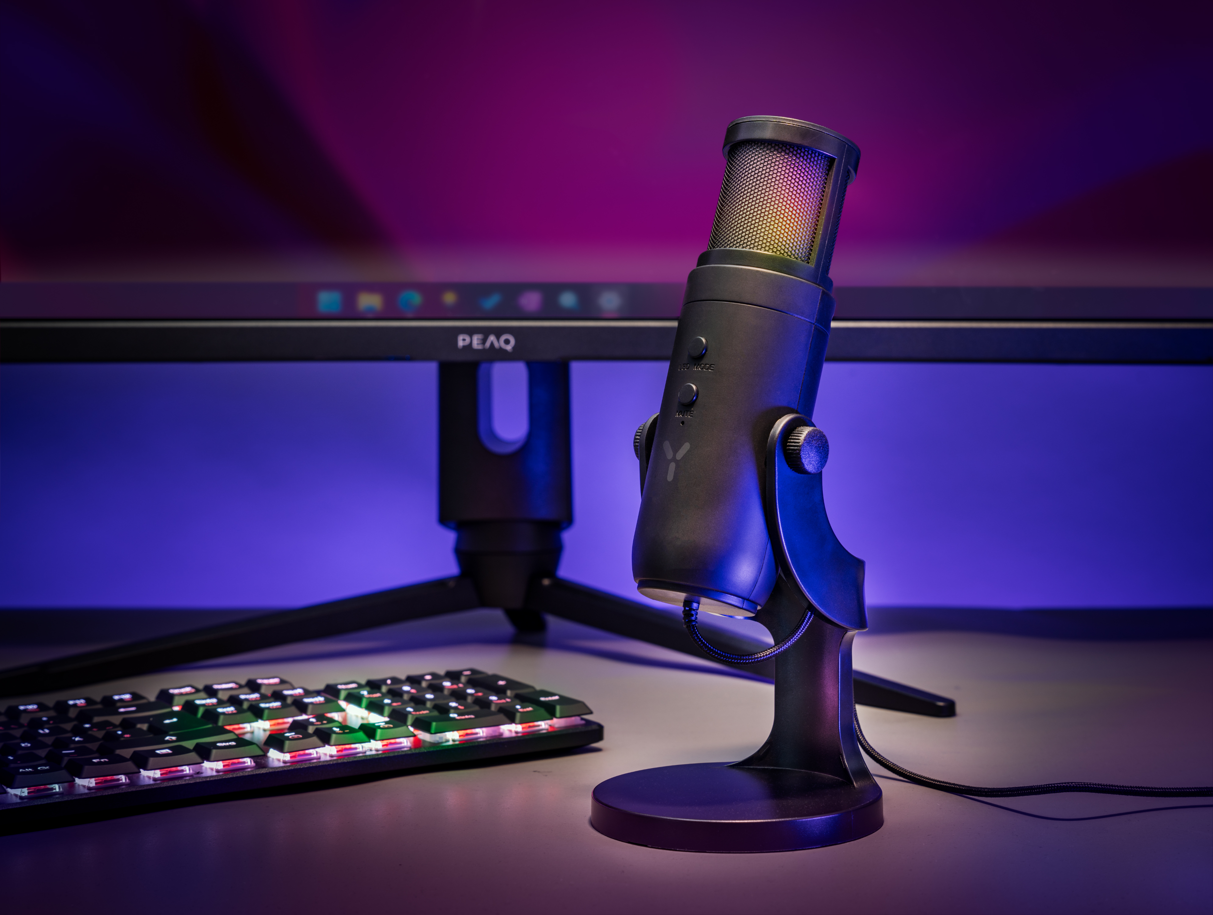 Ein schwarzes Mikrofon auf einem Ständer mit Tastatur und Monitor im Hintergrund.