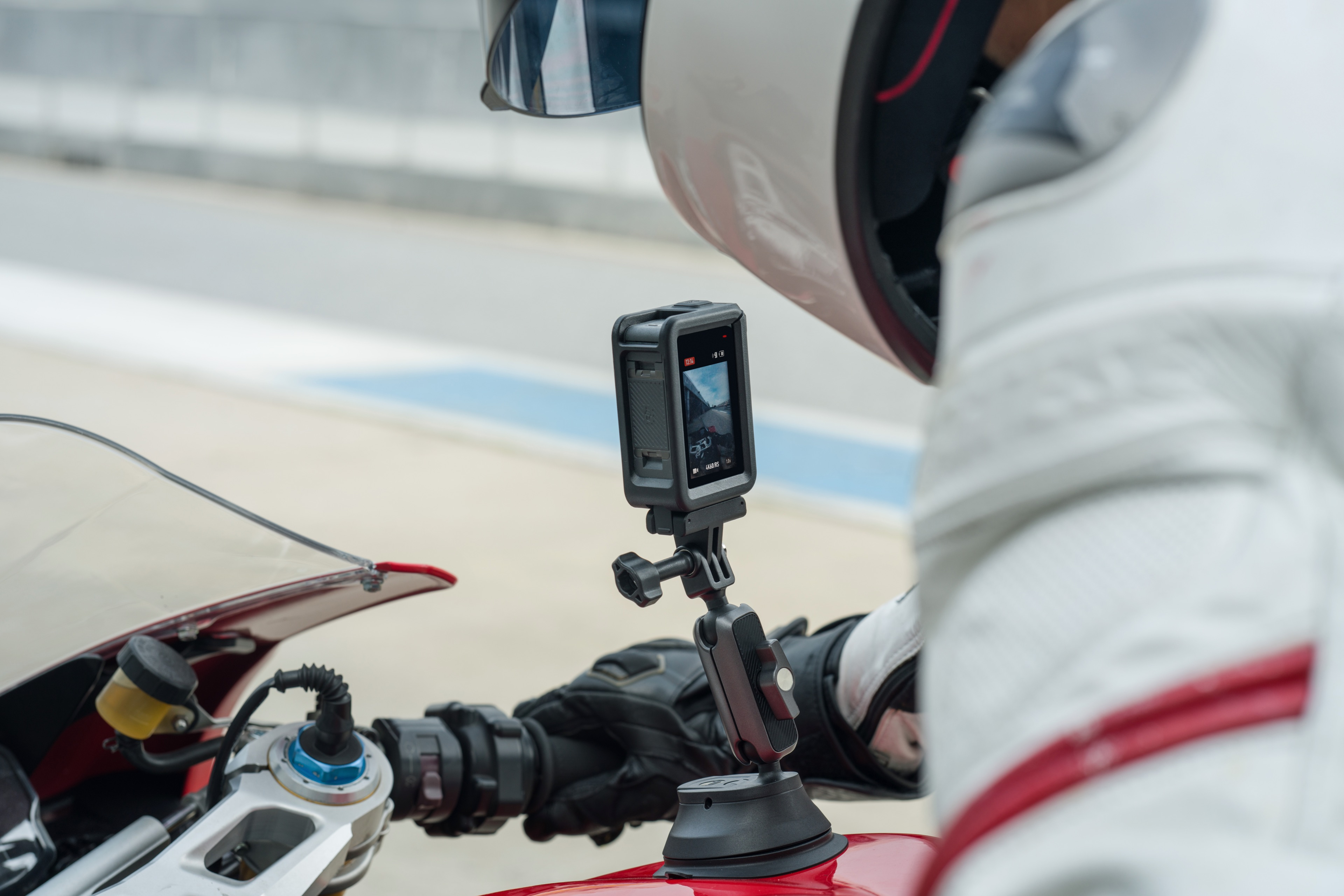 Bir motosiklete monte edilmiş bir GoPro kamerası. Yarış kıyafetleri giymiş bir kişi motosikletin yanında.