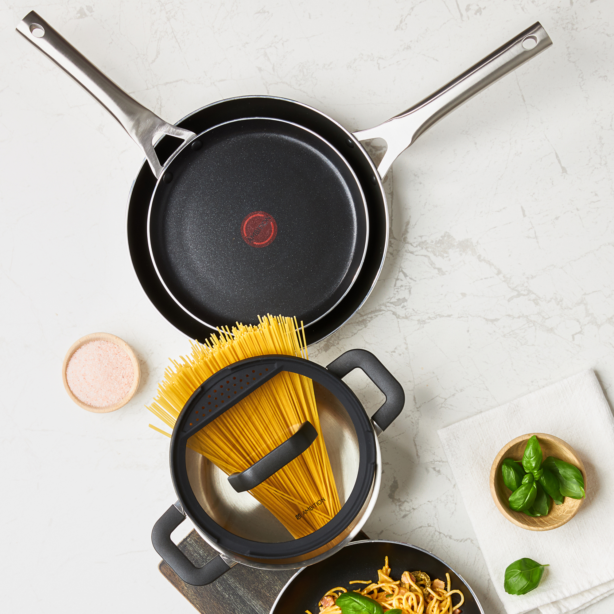 Patelnie i garnek z produktami spożywczymi na białym marmurowym tle, widok z góry.