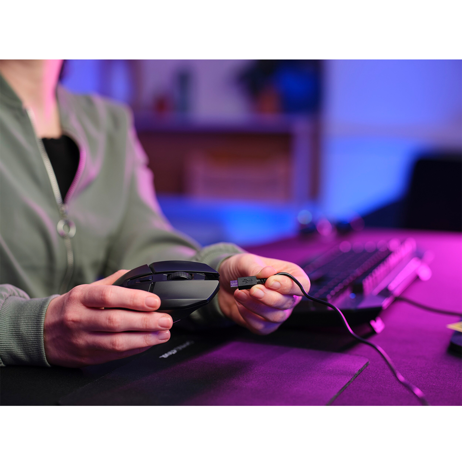 Mani che tengono un mouse nero collegato via USB, vicino a una tastiera su un tappetino nero.