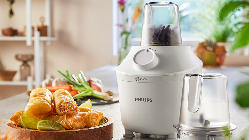 Fehér Philips turmixgép tál tavaszi tekercsekkel és lime szeletekkel egy fa deszkán. Háttérben konyha.