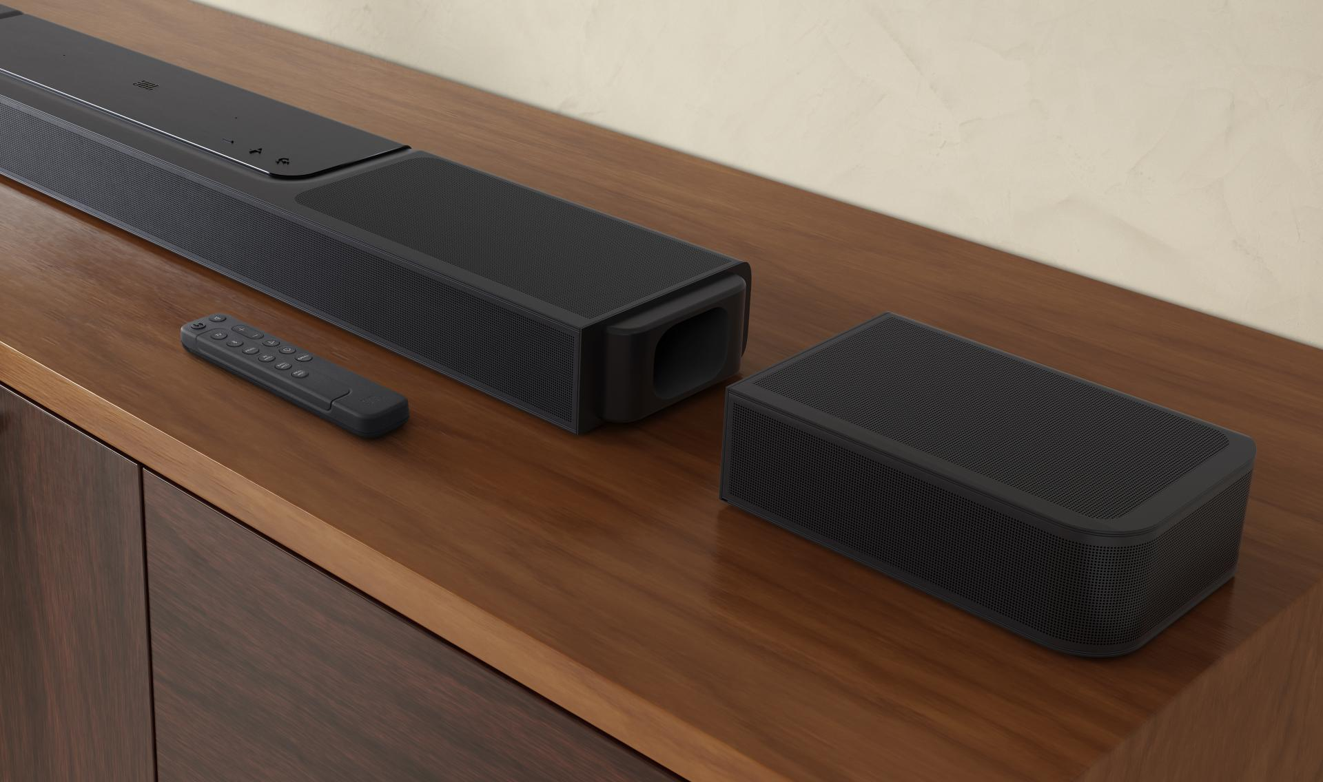 Czarny soundbar, pilot i subwoofer na drewnianym stole. Tło to jasna ściana.