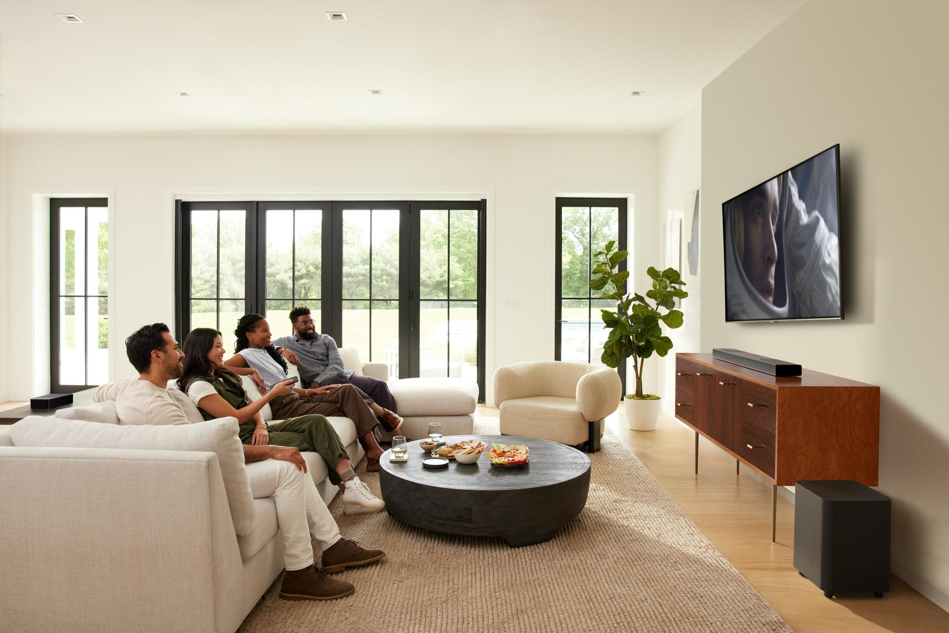 Cztery osoby na kanapie oglądają telewizję w nowoczesnym, jasnym salonie.