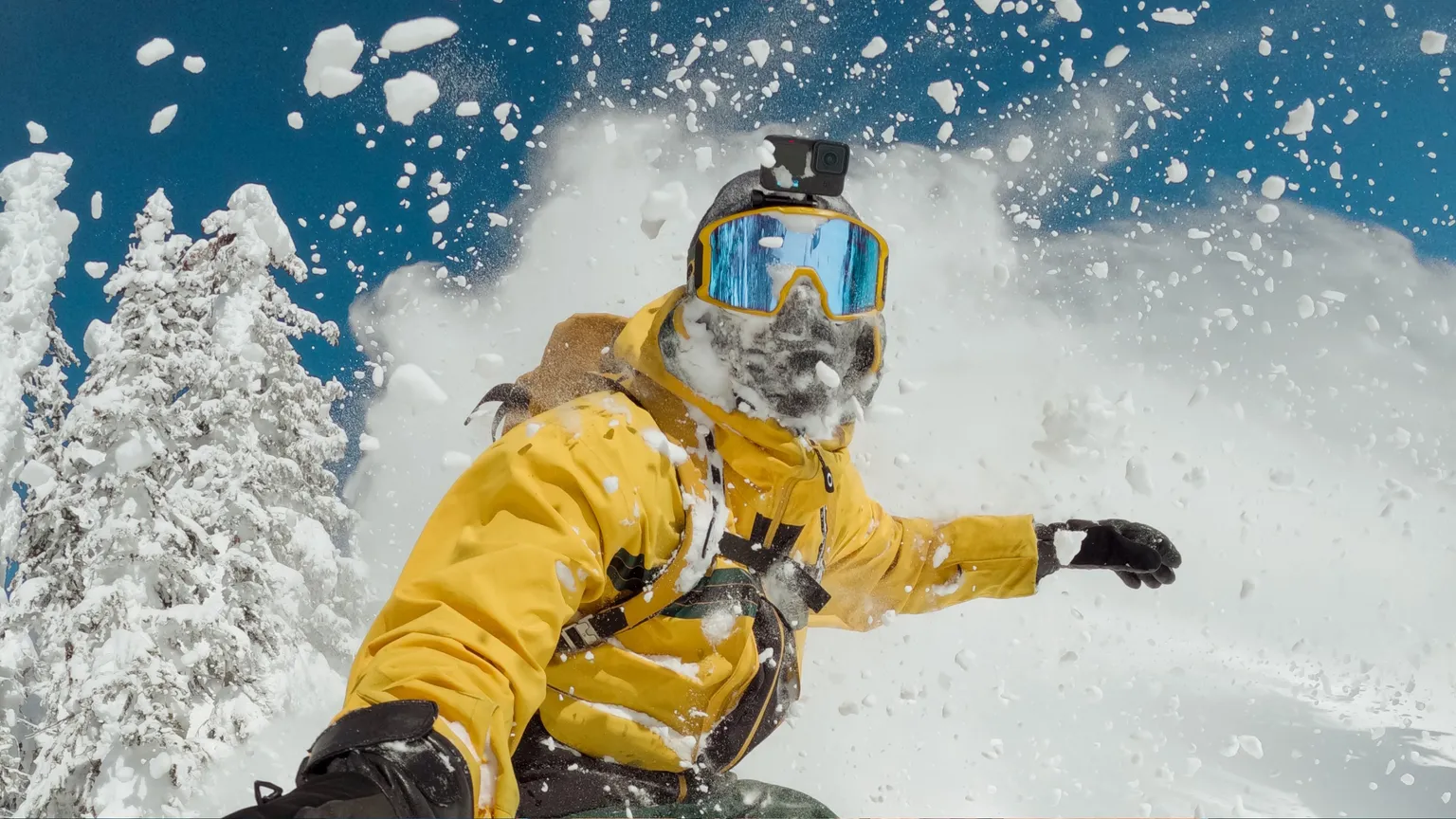 Skieur en veste jaune dans la poudreuse, neige projetée.